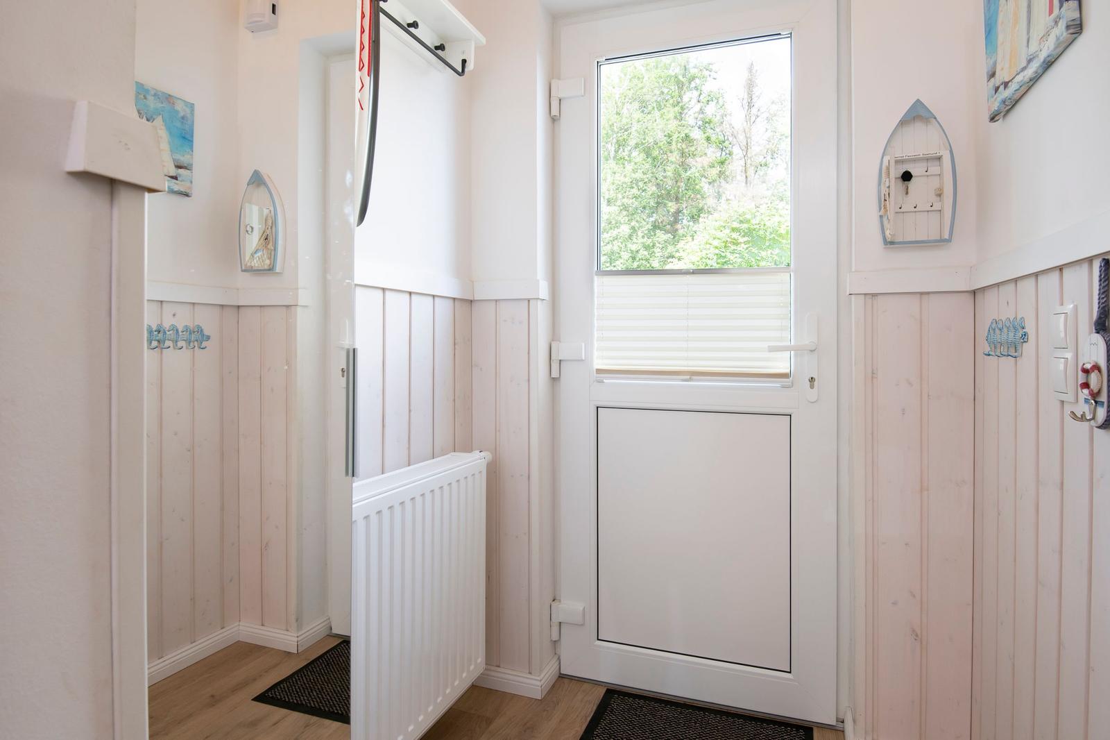 Eingangsbereich mit weißen Wänden, Holzverkleidung und Fenster zur Außenseite.