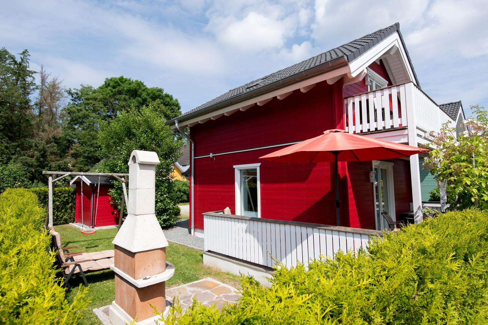 Rotes Haus mit Balkon, Terrasse und Garten. Roter Sonnenschirm und Grillplatz.