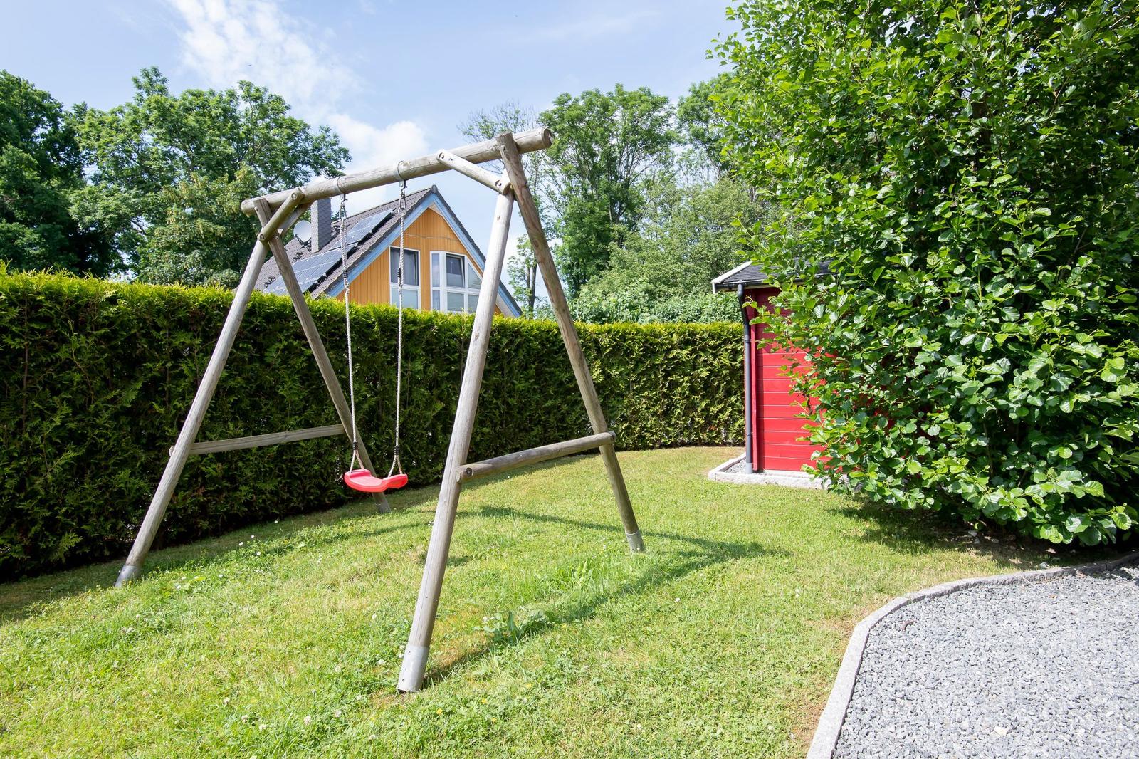 Hinterhof mit Schaukel, Rasenfläche und rotem Gartenhaus. Im Hintergrund ist ein Haus mit Solaranlage zu sehen.