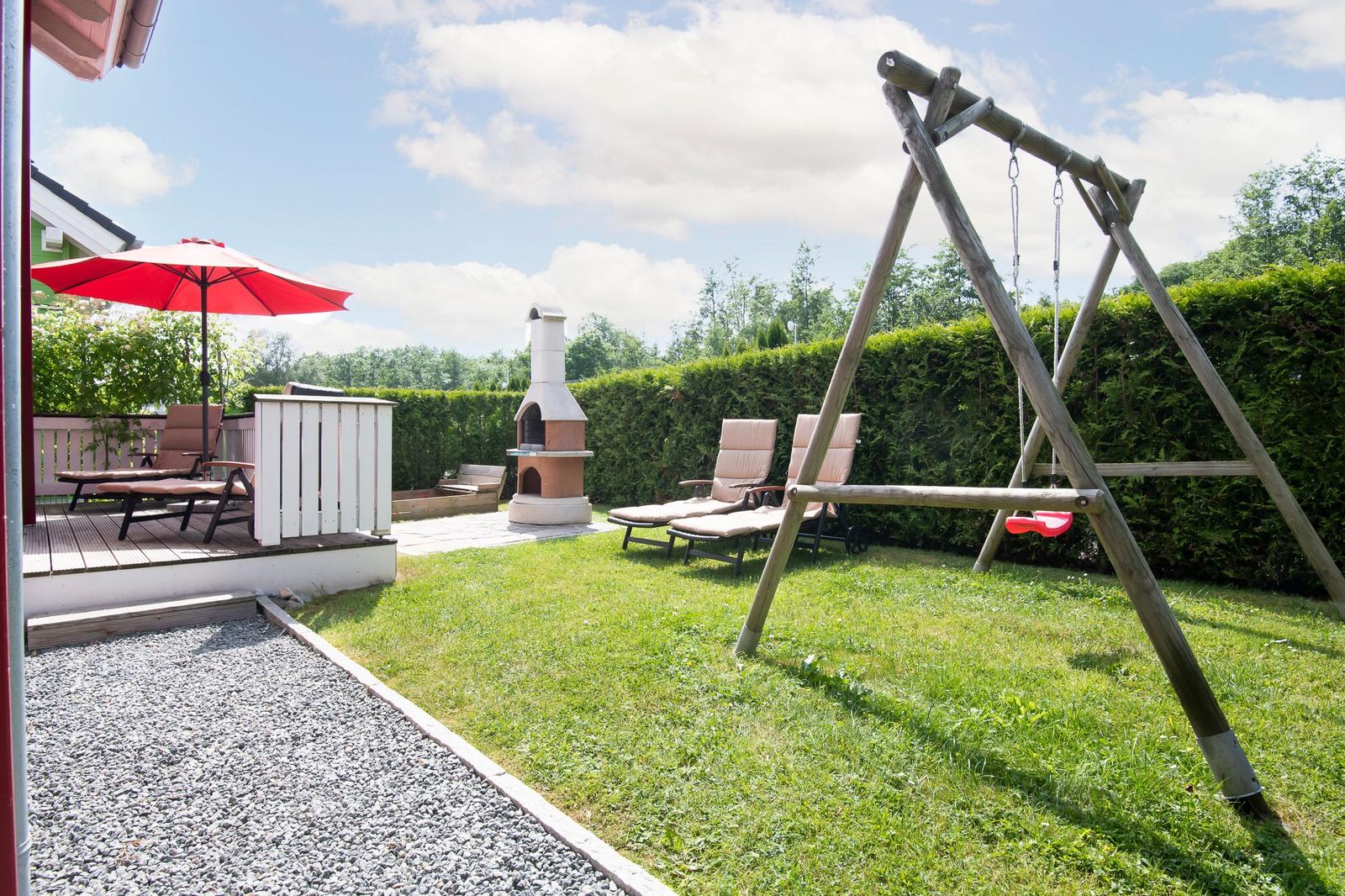 Hinterhof mit Grill, Liegestühlen, Schaukel und rotem Sonnenschirm.