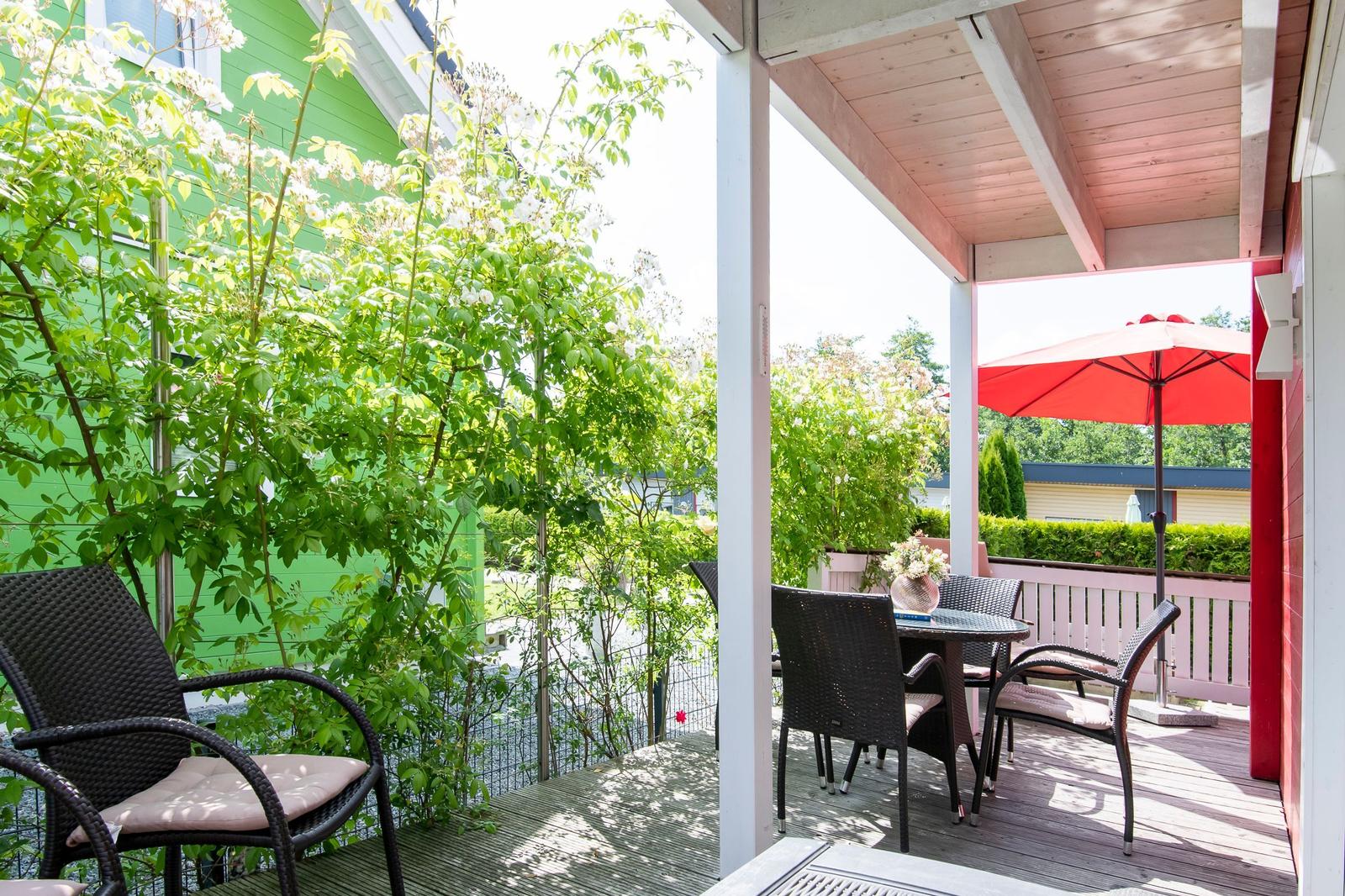 Terrasse mit Tisch, Stühlen und rotem Sonnenschirm. Grün bewachsene Wand im Hintergrund.