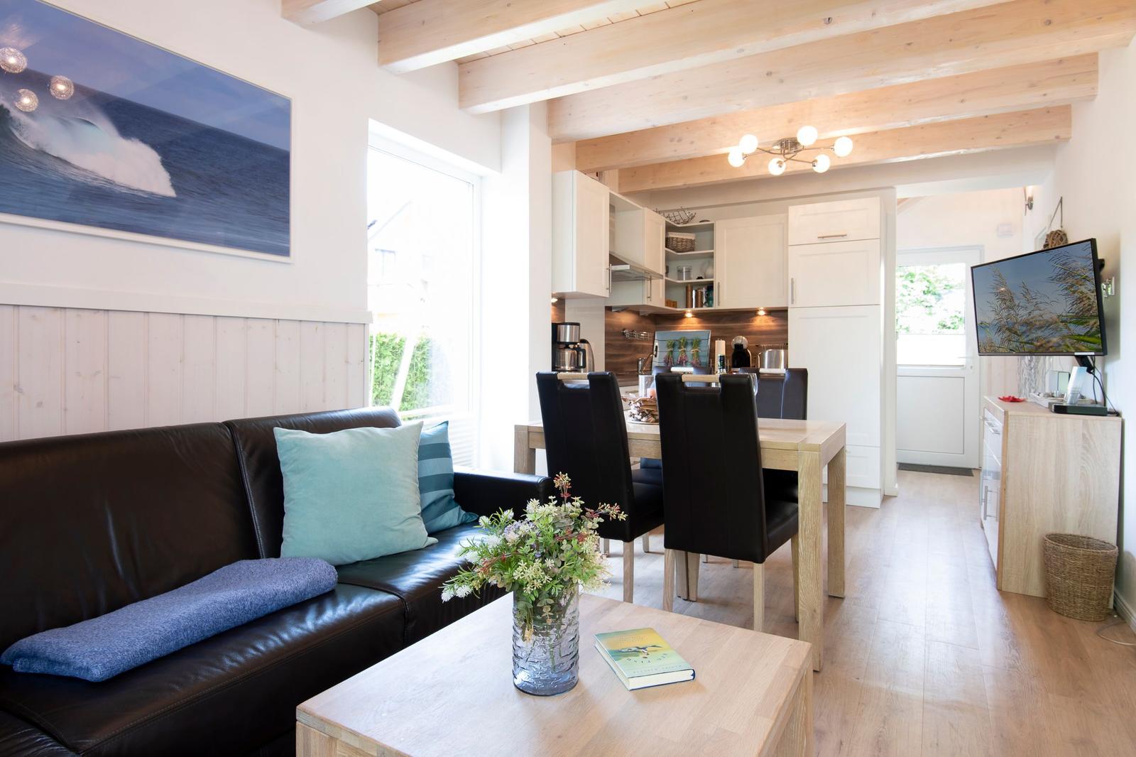 Wohnzimmer mit Sofa, Esstisch und Küche im Hintergrund. Holzbalken und Wandverkleidung.