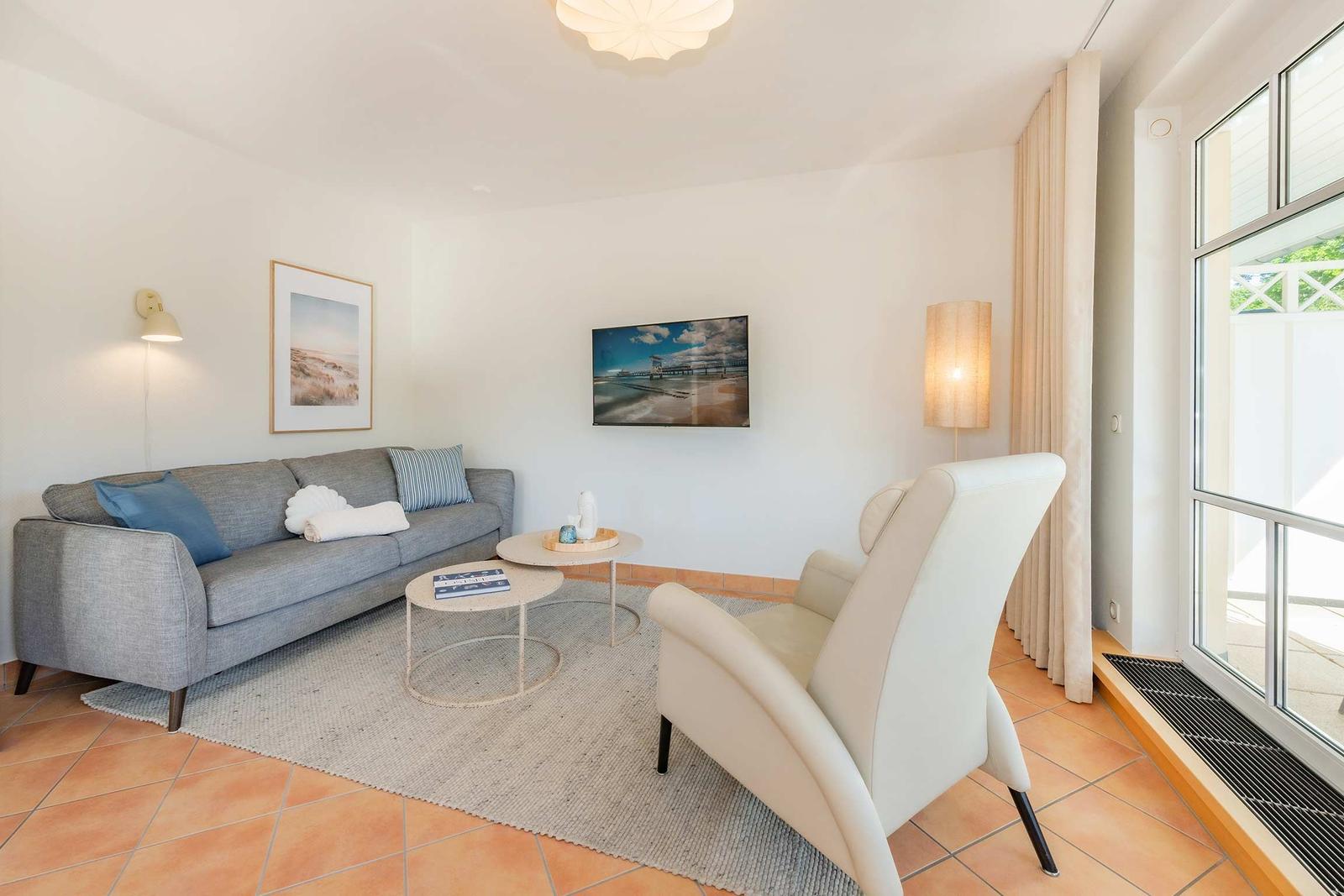 Wohnzimmer mit Sofa, Sessel, Couchtisch und Fernseher an der Wand.