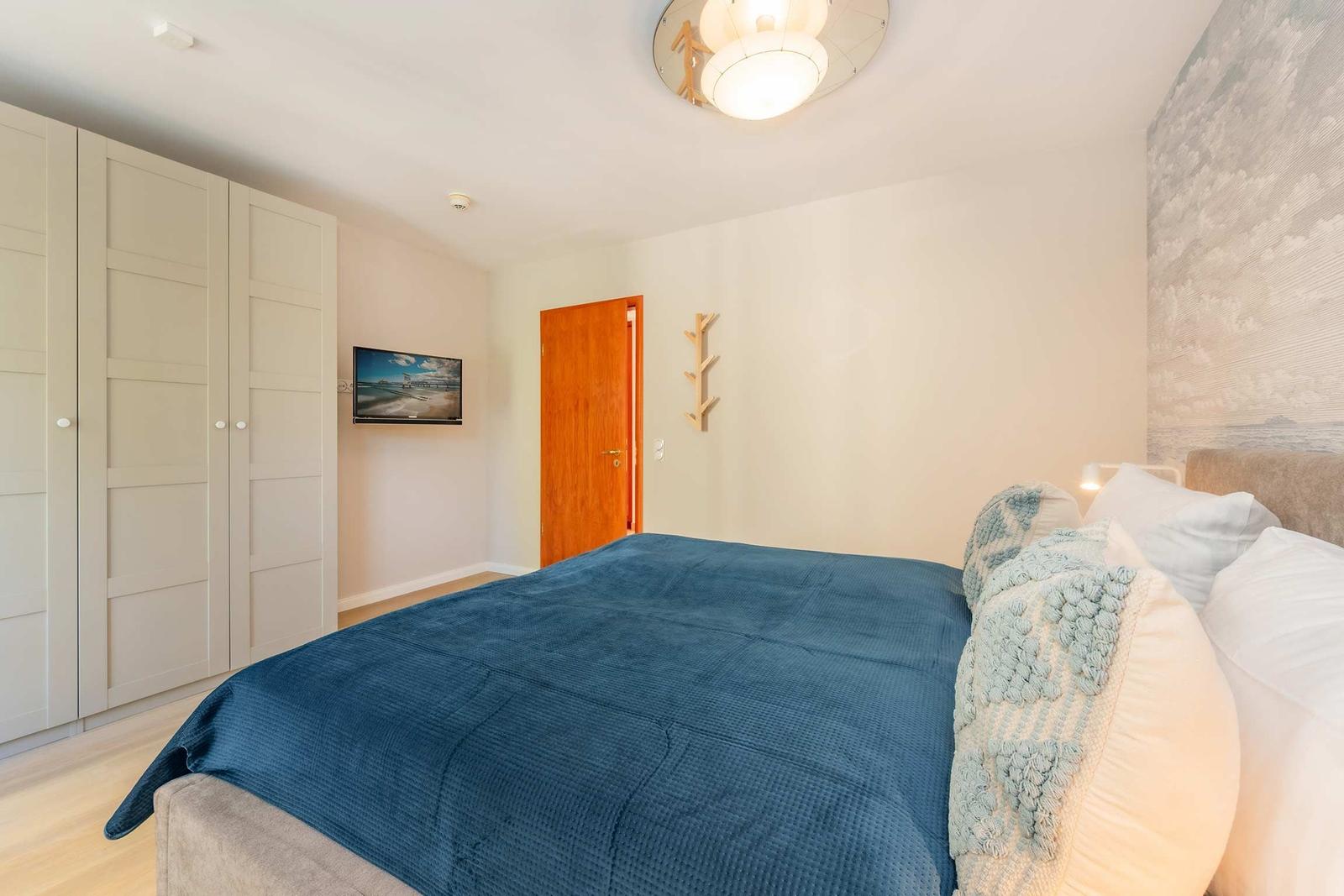 Schlafzimmer mit Bett, Kleiderschrank und Wand-TV.