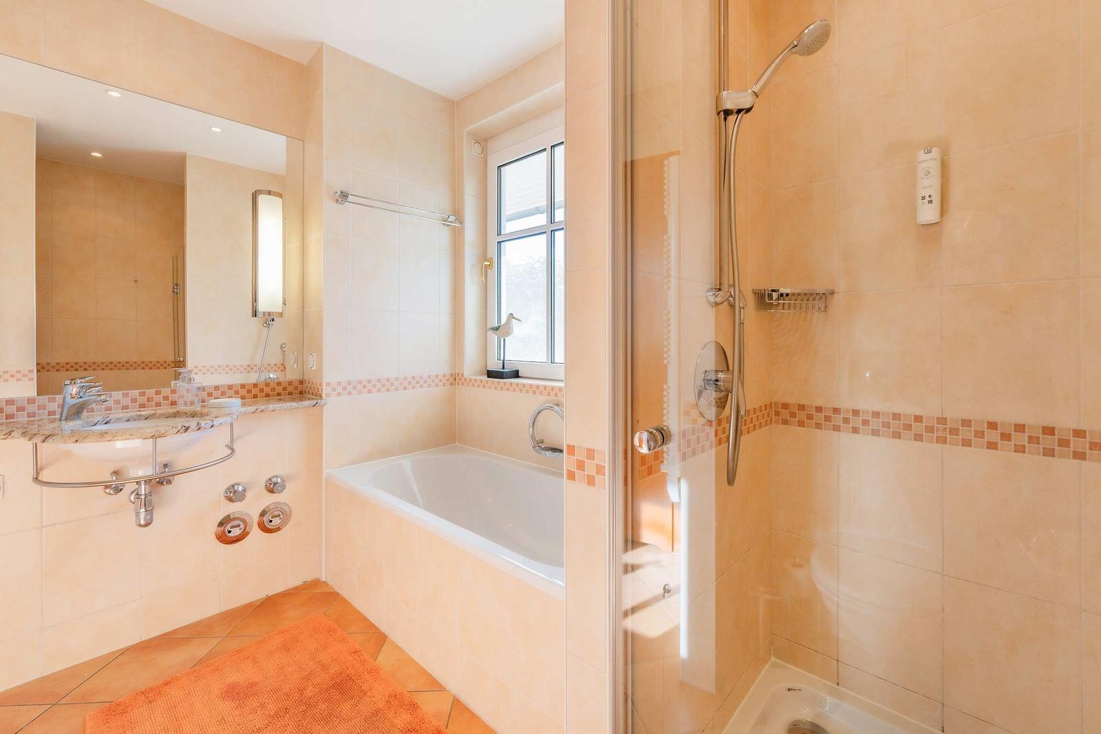 Bad mit Dusche, Badewanne und Waschbecken. Fenster, Spiegel und Bodenfliesen.