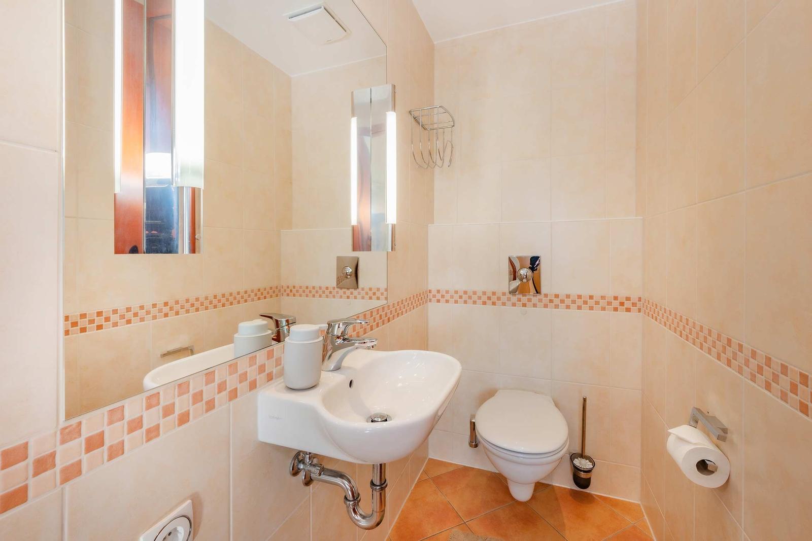 Badezimmer mit Waschbecken, Spiegel, Toilette und Fliesenverkleidung.
