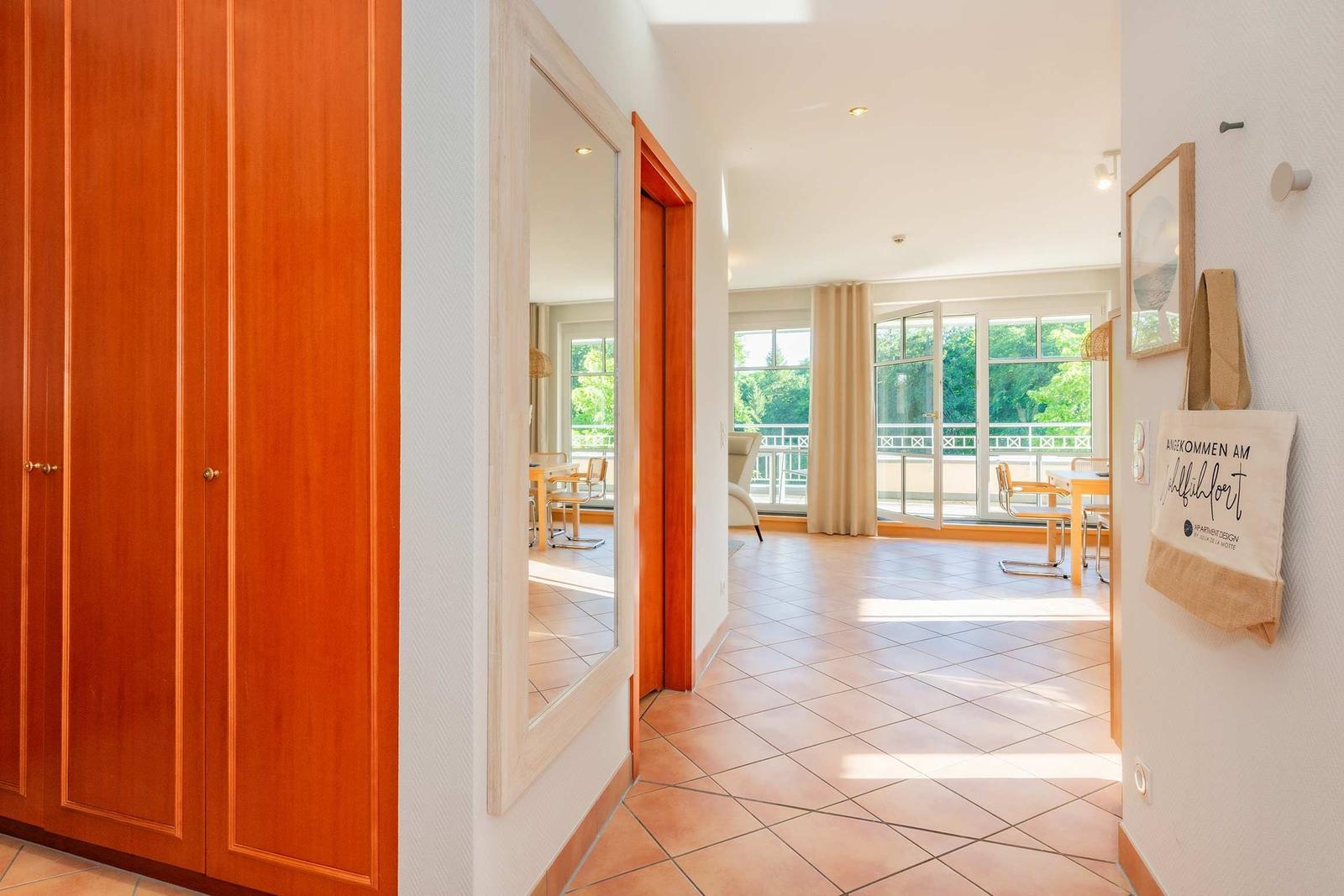 Flur mit Holzschrank, Spiegel und Blick in Wohnbereich mit Terrasse.