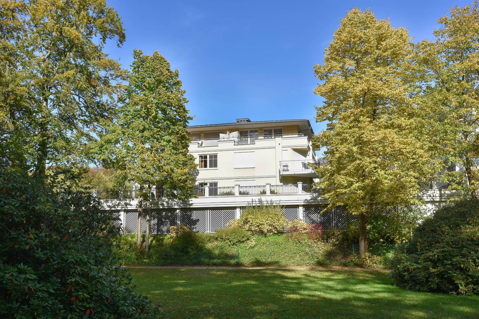 Ein mehrstöckiges Haus mit Balkonen und umgeben von Bäumen und Grünflächen.