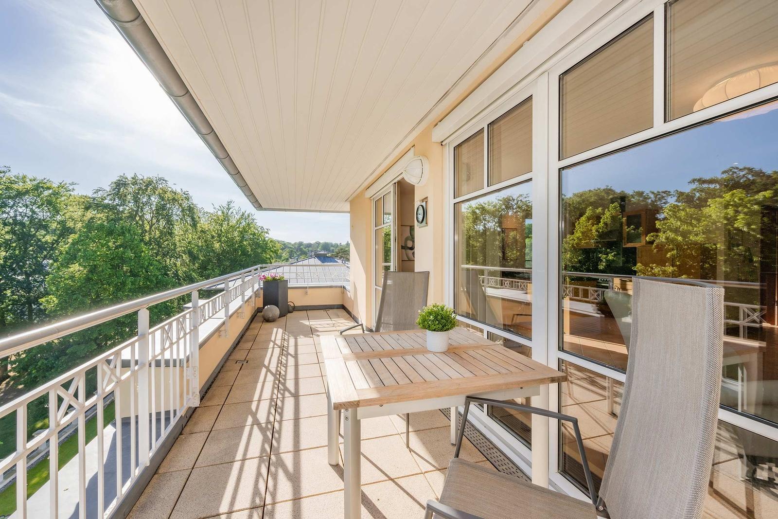 Terrasse mit Tisch, Stühlen und Blick auf grüne Bäume.