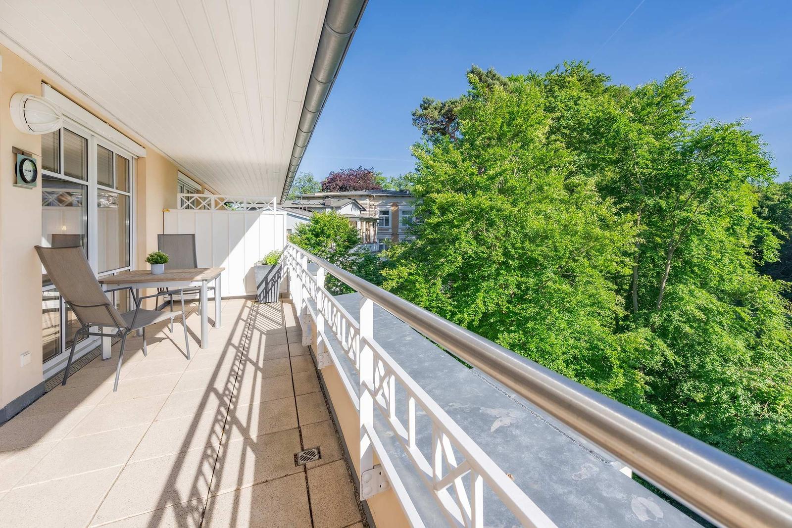 Terrasse mit Tisch und Stühlen, Blick auf grüne Bäume und einen klaren Himmel.