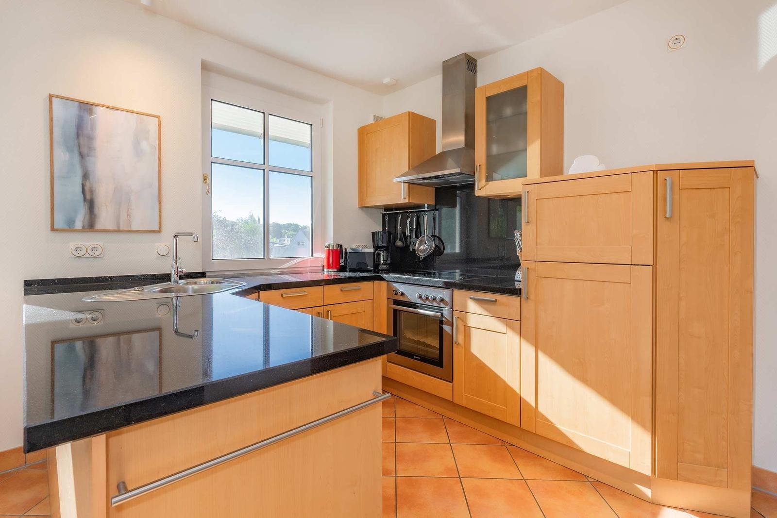 Küche mit Holzschränken, schwarzer Arbeitsplatte und Fenster zum Blick nach draußen.