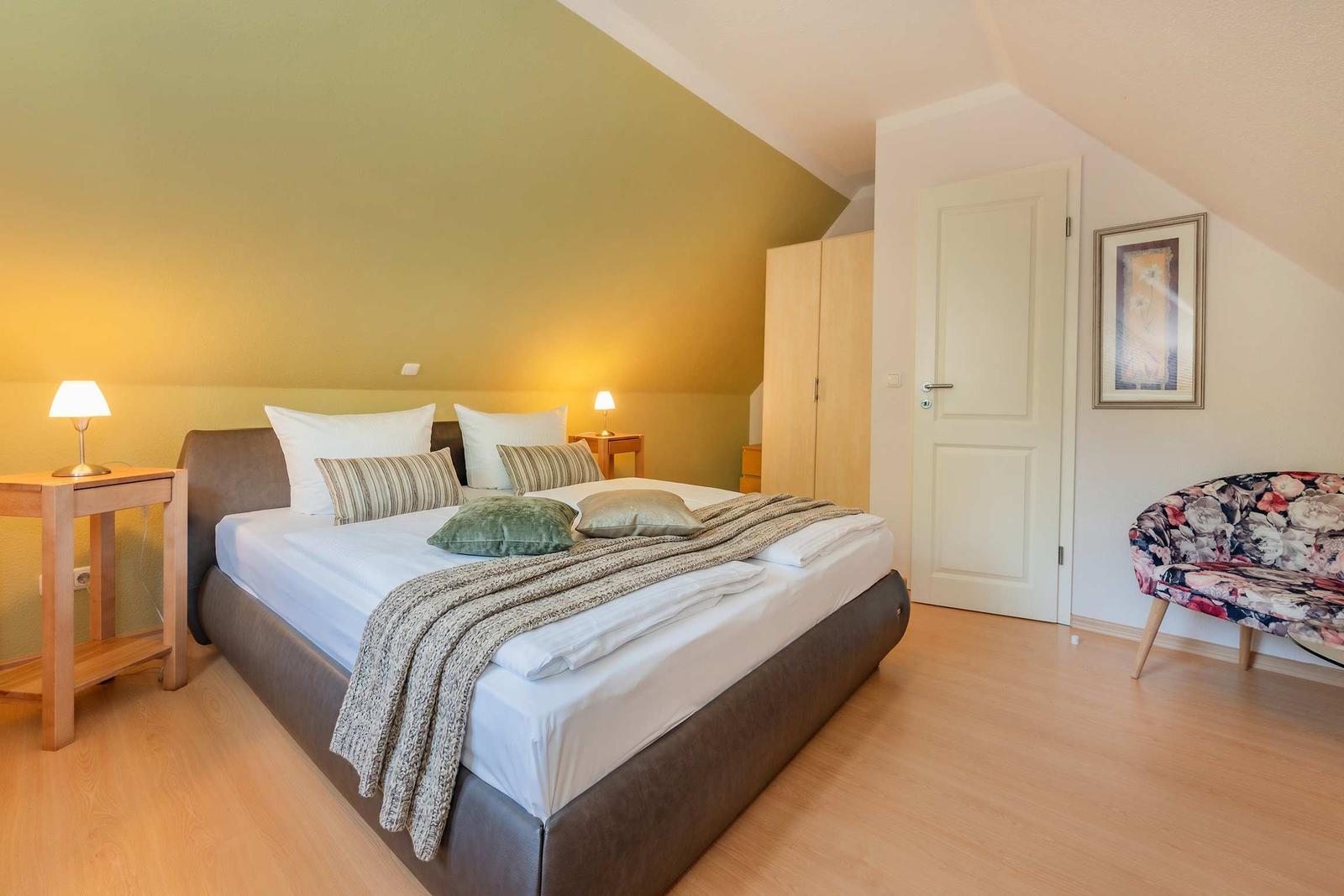 Schlafzimmer mit Doppelbett, Nachttischen, Kleiderschrank und Sessel.
