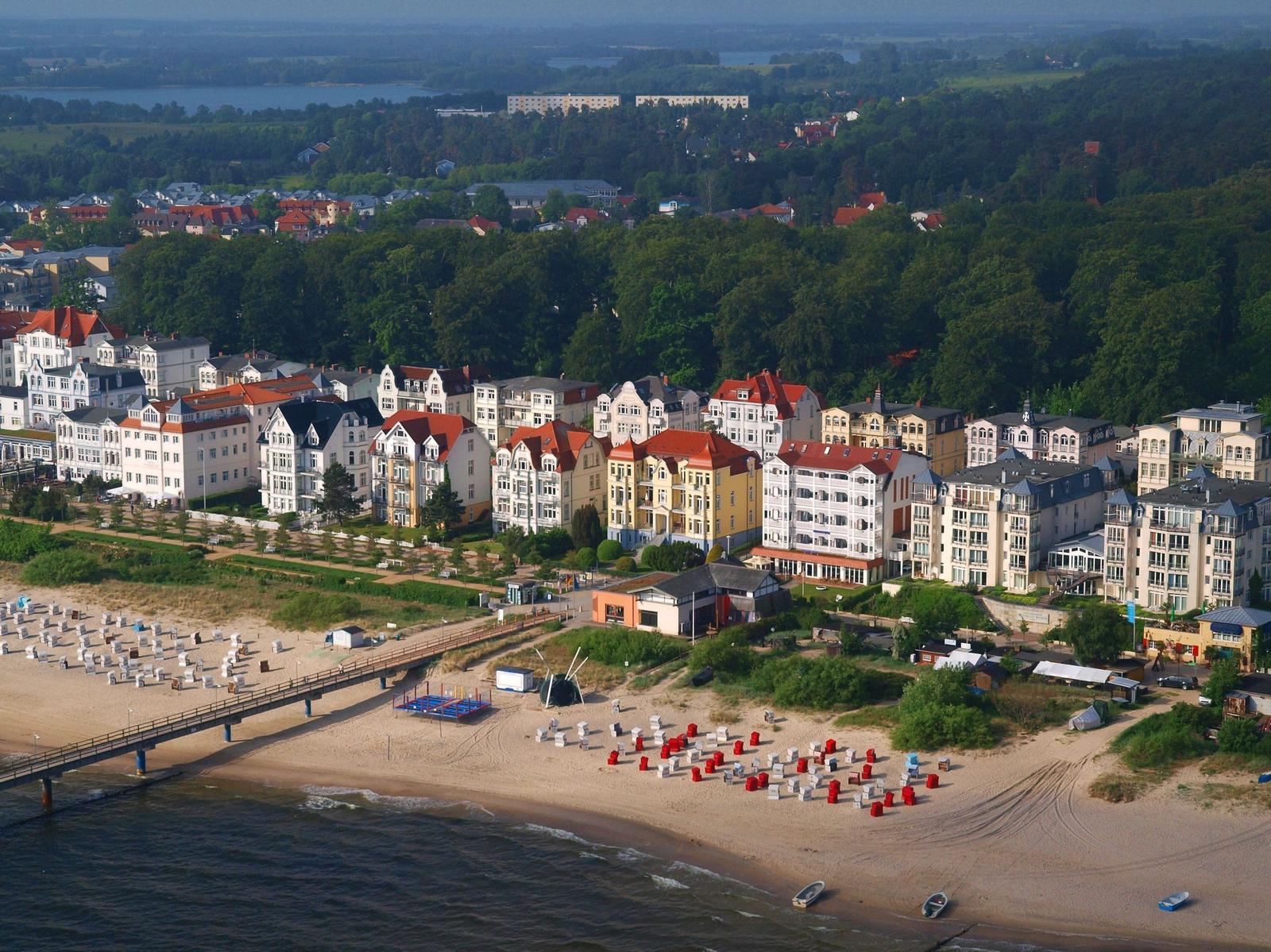 Strand mit Steg und bunten Strandkörben vor historischen Häusern am Wasser.