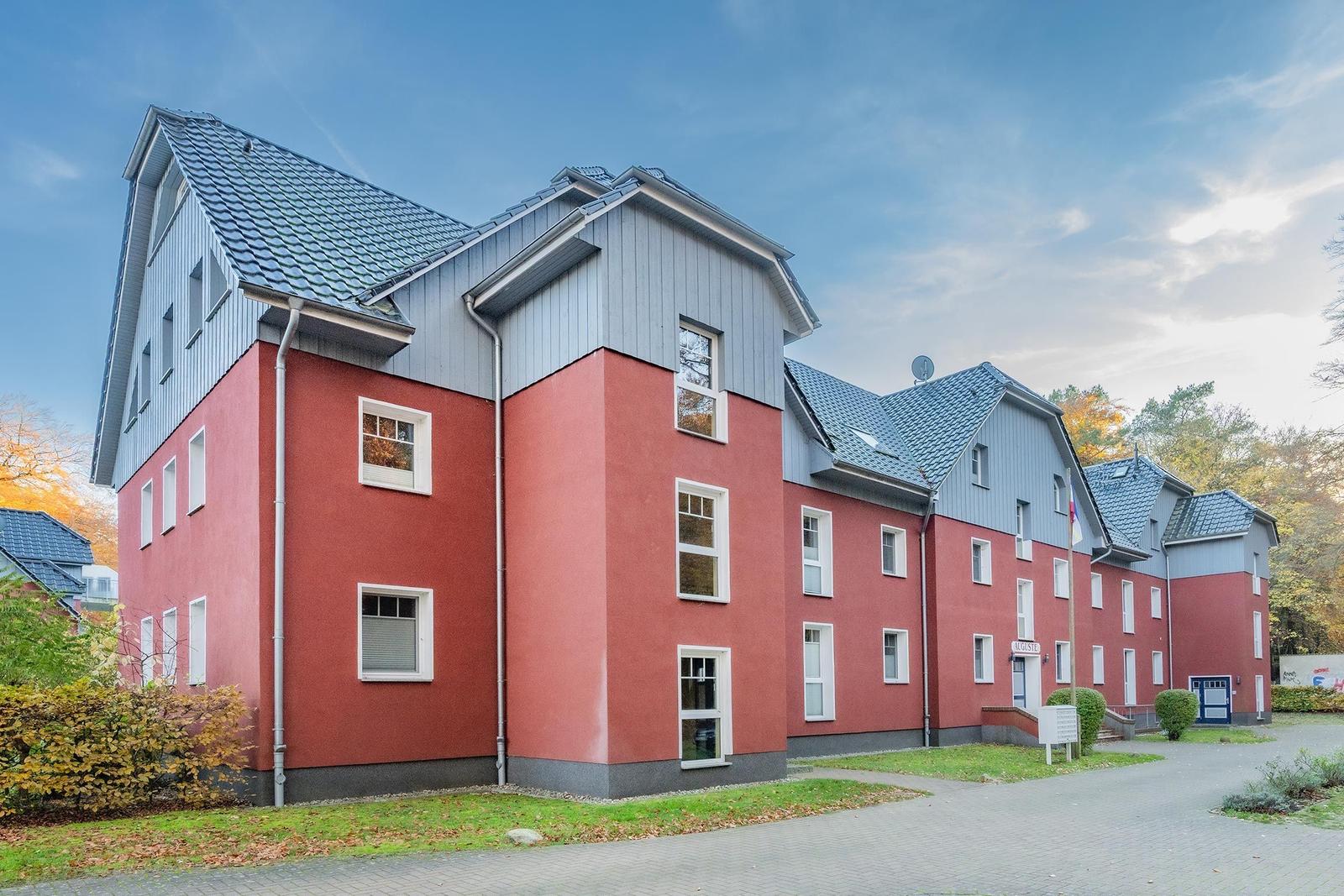 Rotes Mehrfamilienhaus mit grauem Dach und weißen Fenstern.