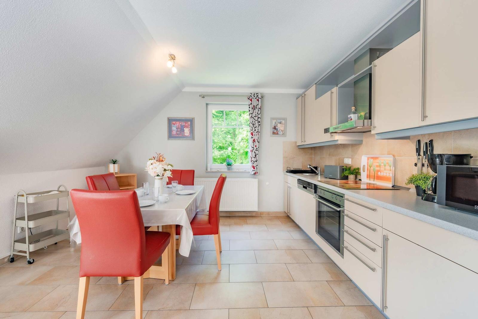 Küche und Essbereich mit roten Stühlen und Fensterblick auf Grün.