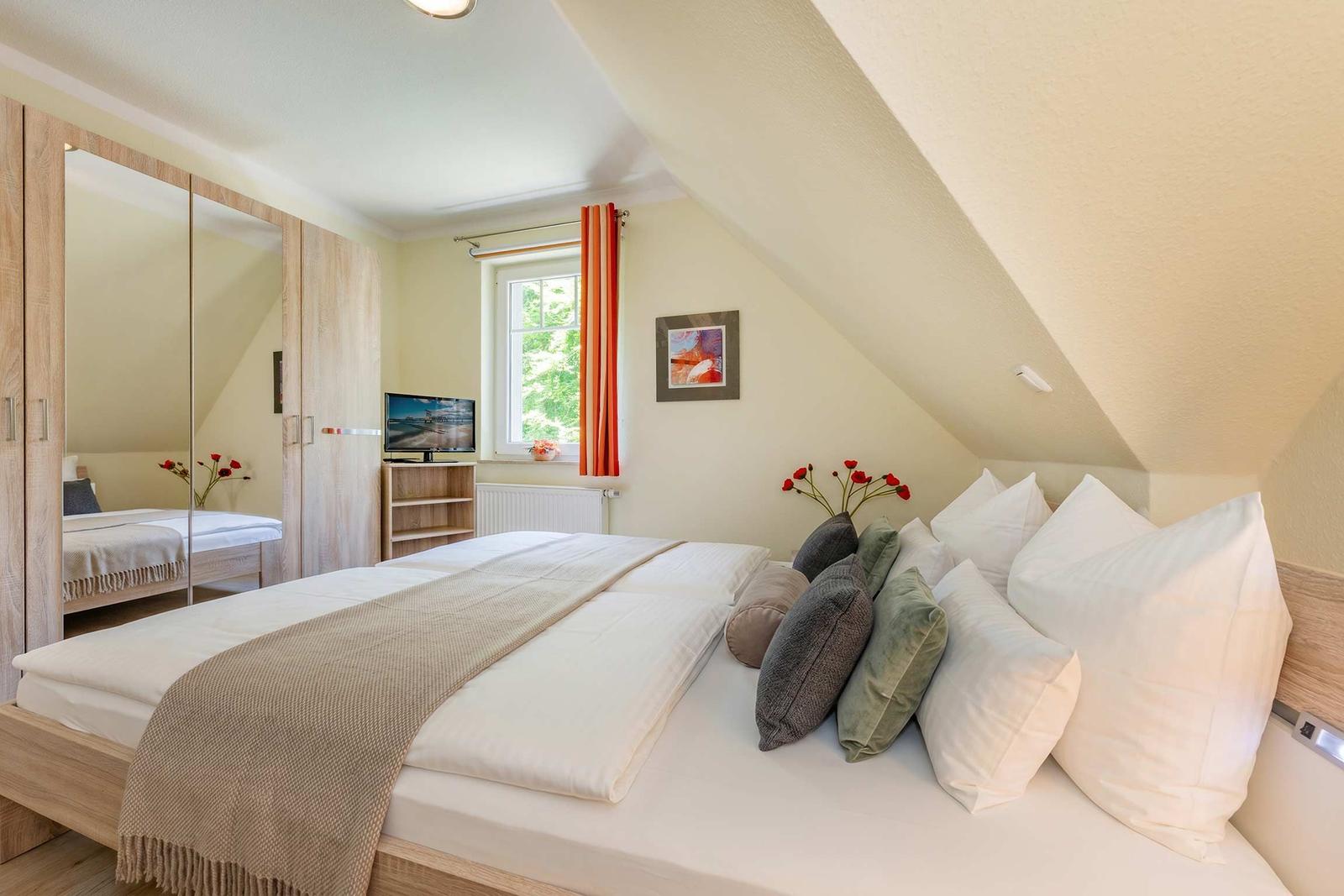 Schlafzimmer mit Dachschrägen, Bett, Kleiderschrank, Fenster und Fernseher.