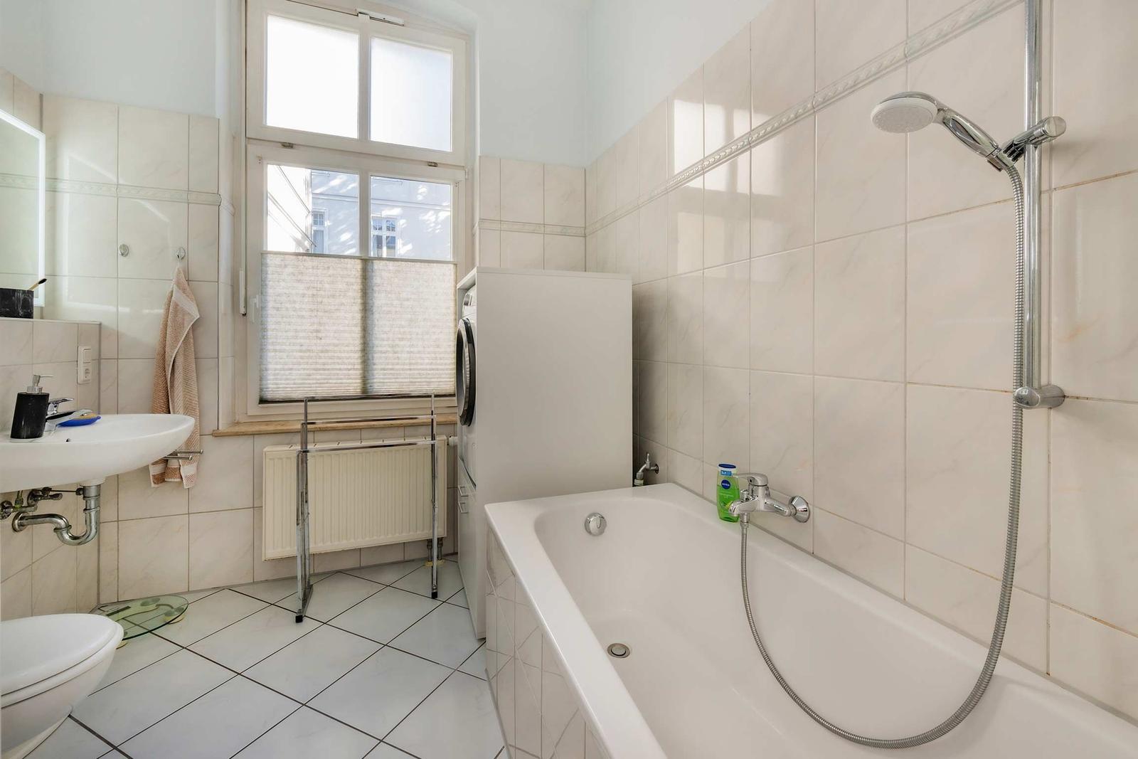 Badezimmer mit Badewanne, Dusche, Waschmaschine und Fenster.