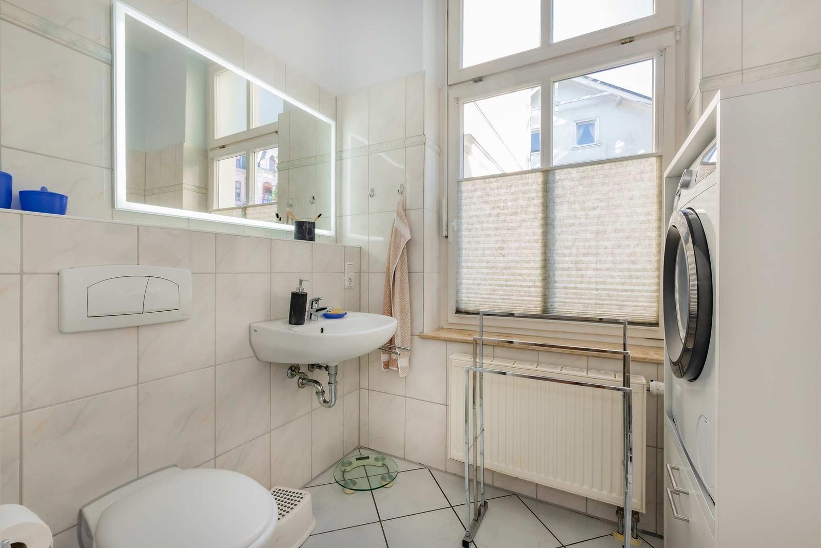 Badezimmer mit Waschmaschine, Spiegel und Fenster