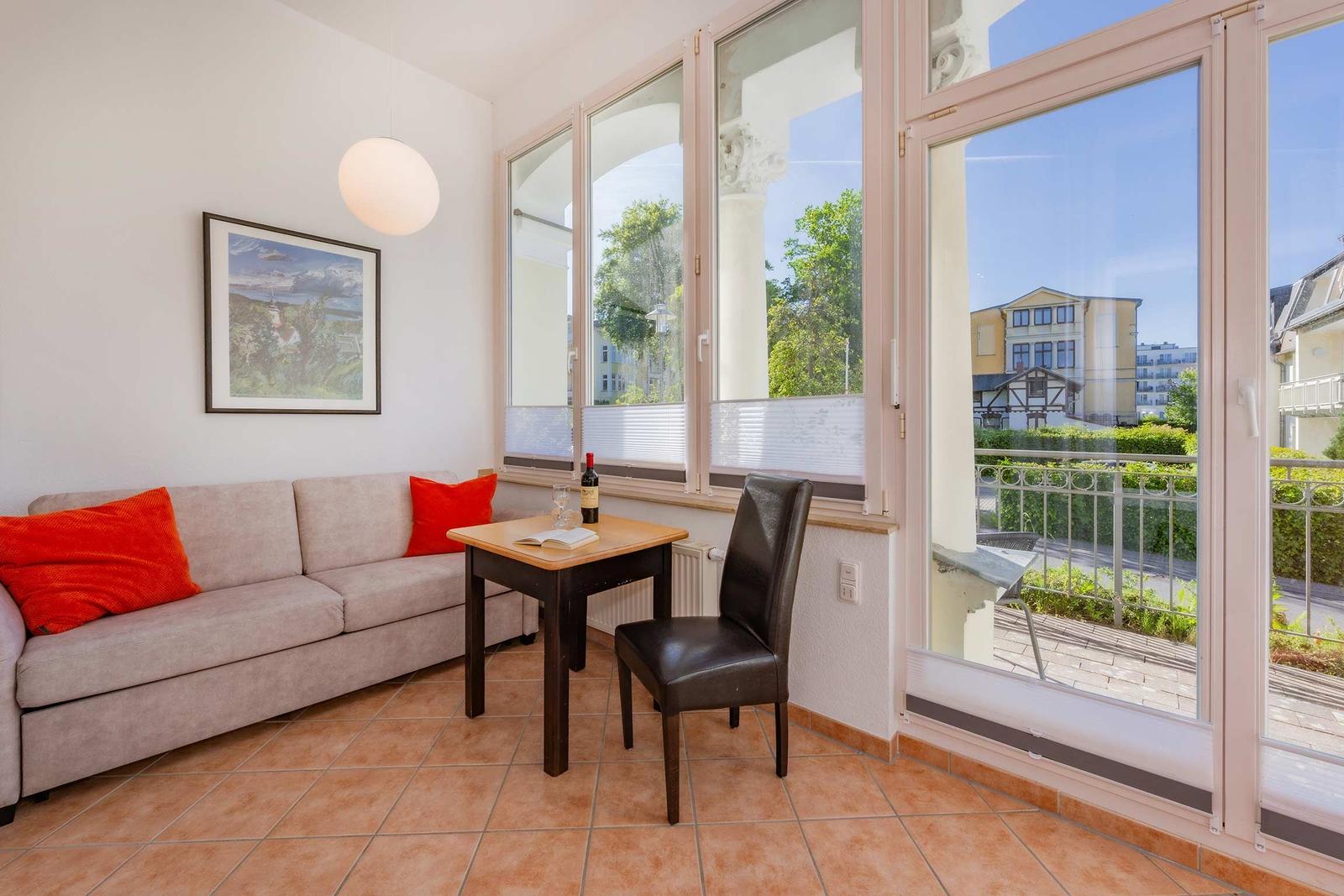 Wohnzimmer mit Sofa, Tisch und Stuhl. Balkon mit Blick auf Grünflächen.