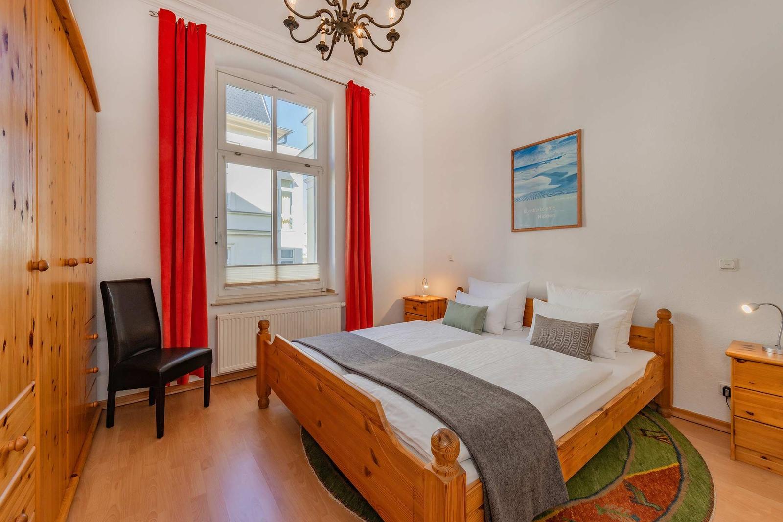 Schlafzimmer mit Holzbett, roten Vorhängen und Holzmöbeln.