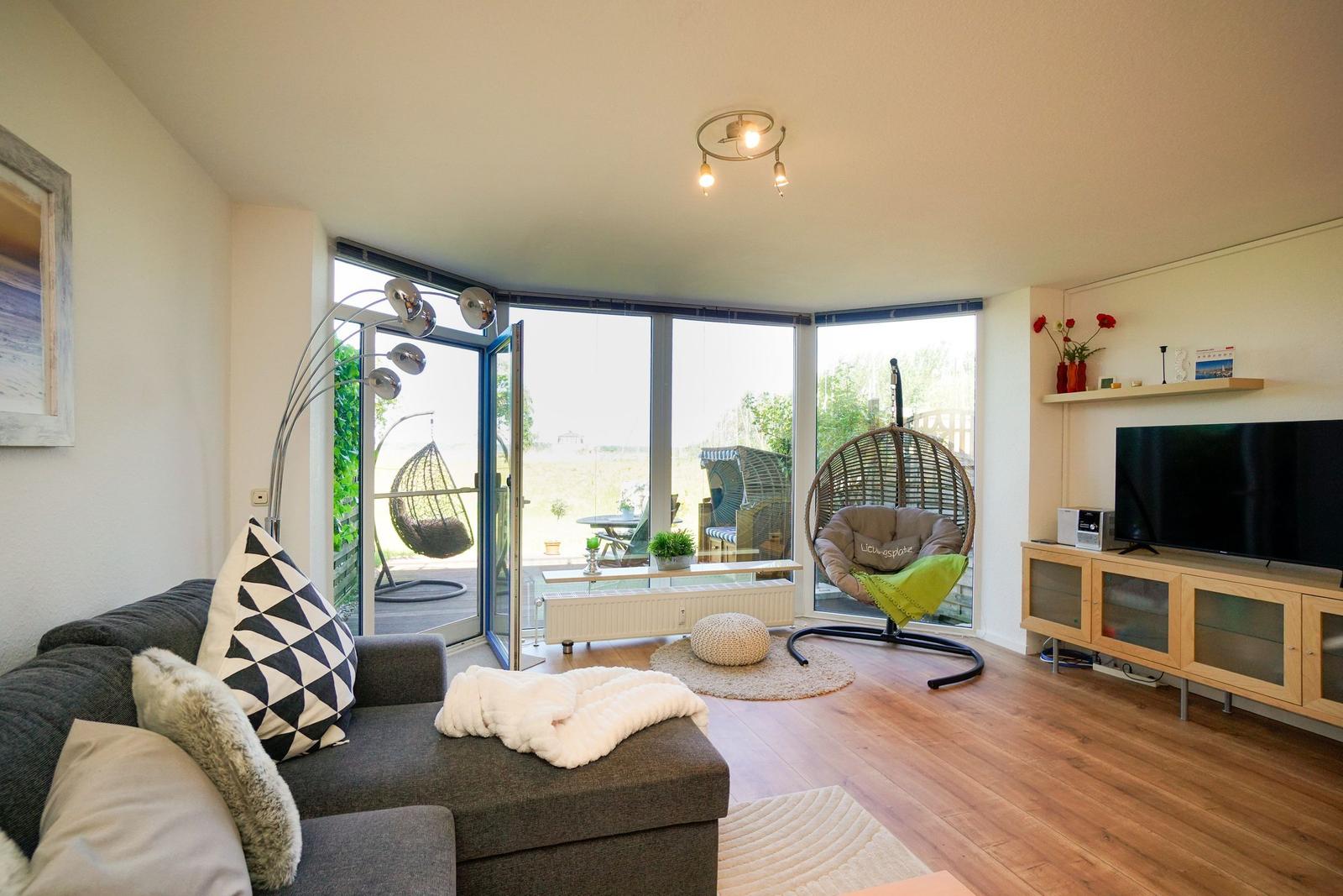 Wohnzimmer mit Sofa, TV und Terrasse mit Hängesessel.