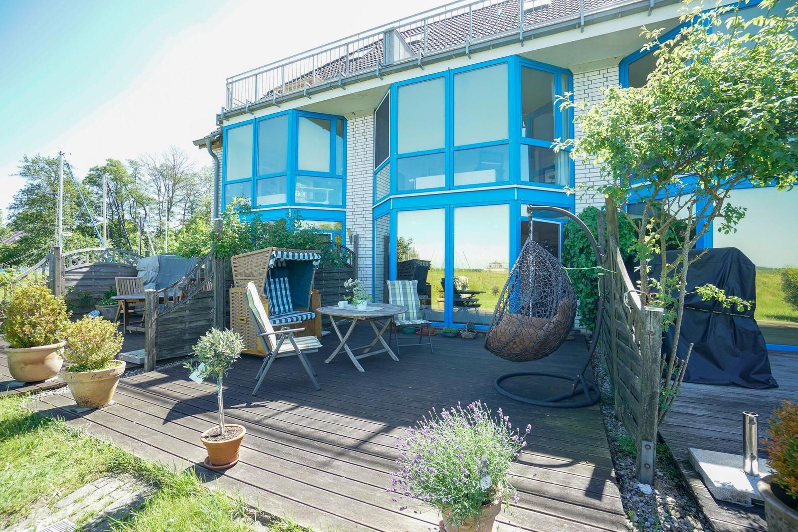 Terrasse mit Sitzgelegenheiten und Pflanzen vor einem Haus mit blauen Fenstern.