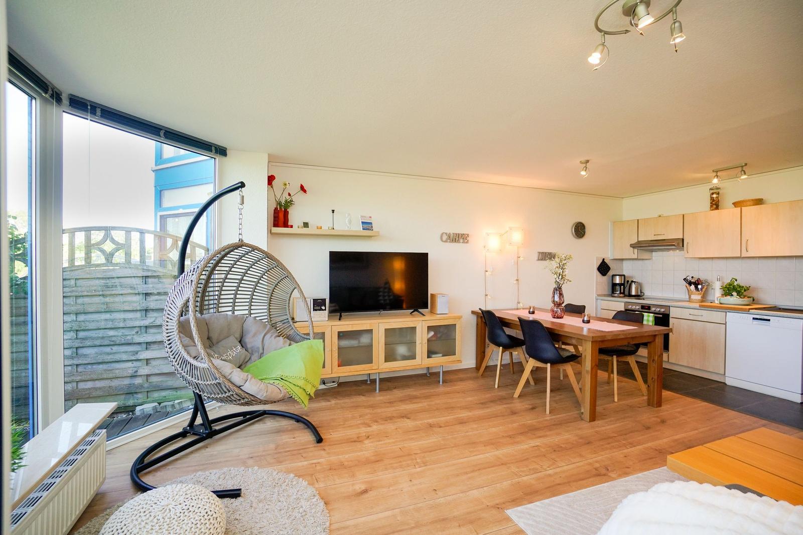 Wohn- und Essbereich mit TV, Esstisch und Küche. Hängesessel und Holzboden.
