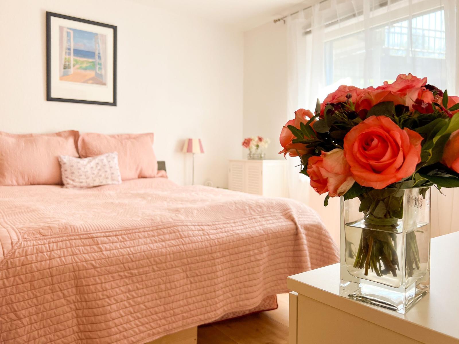Schlafzimmer mit Bett, Blumen und Bild an der Wand.