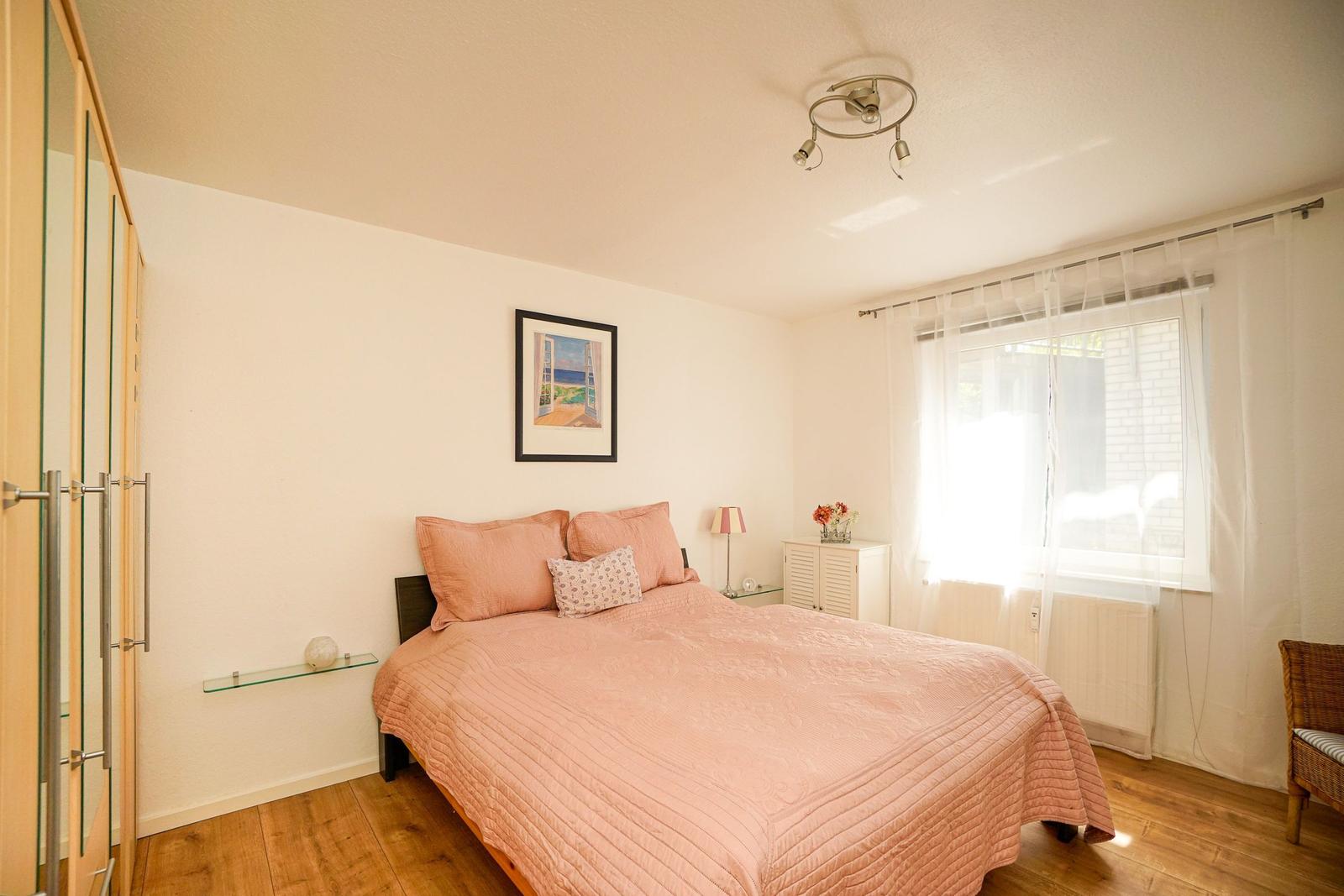 Schlafzimmer mit Bett, Schrank und Fenster. Wandbild und Beleuchtung sichtbar.