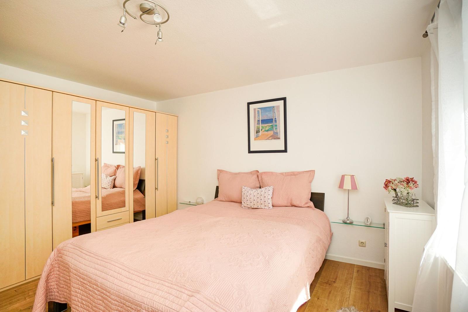 Schlafzimmer mit Bett, Schrank und Nachttisch. Wandbild und Blumen.