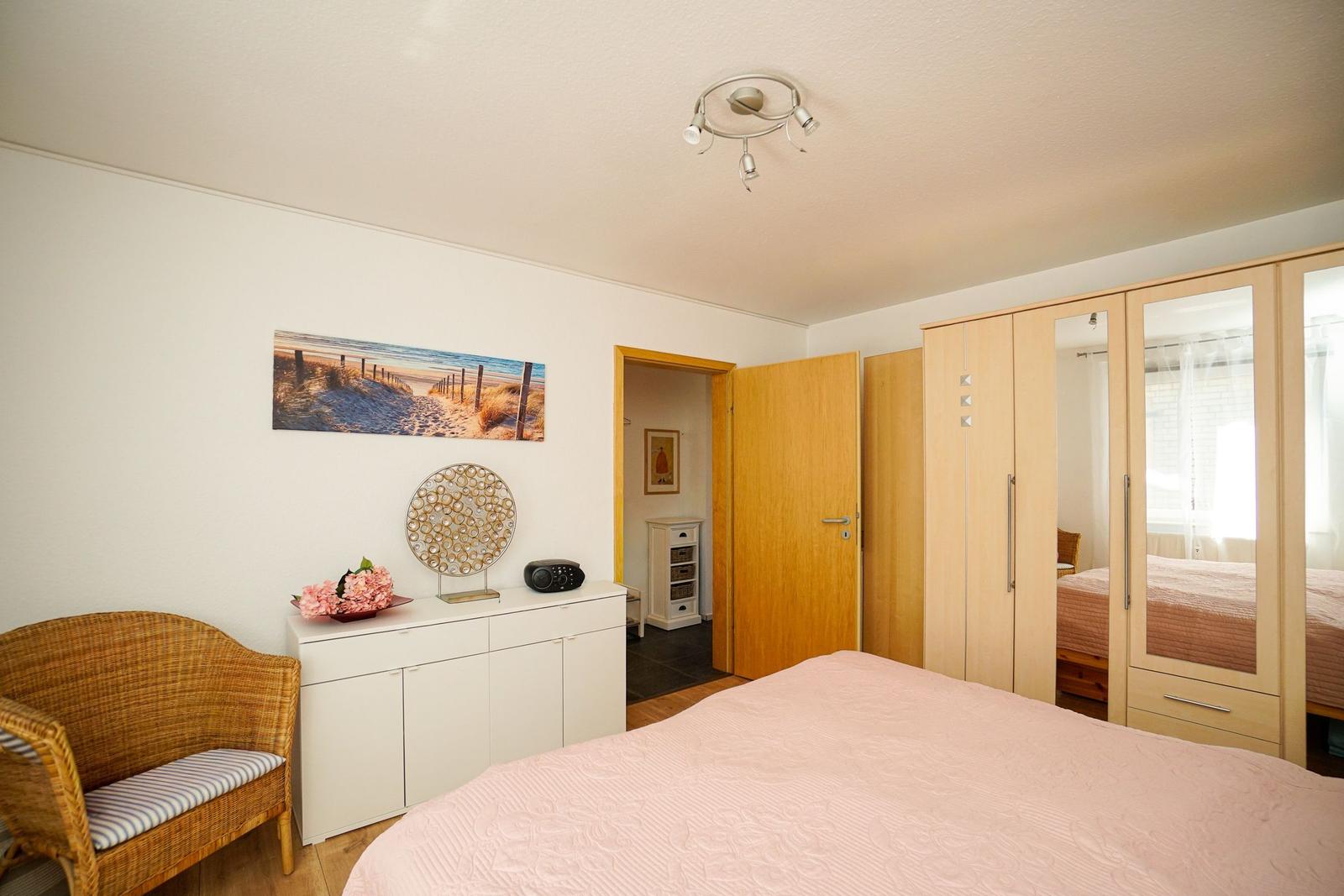 Schlafzimmer mit Bett, Schrank und Stuhl. Wandbild zeigt Strand.