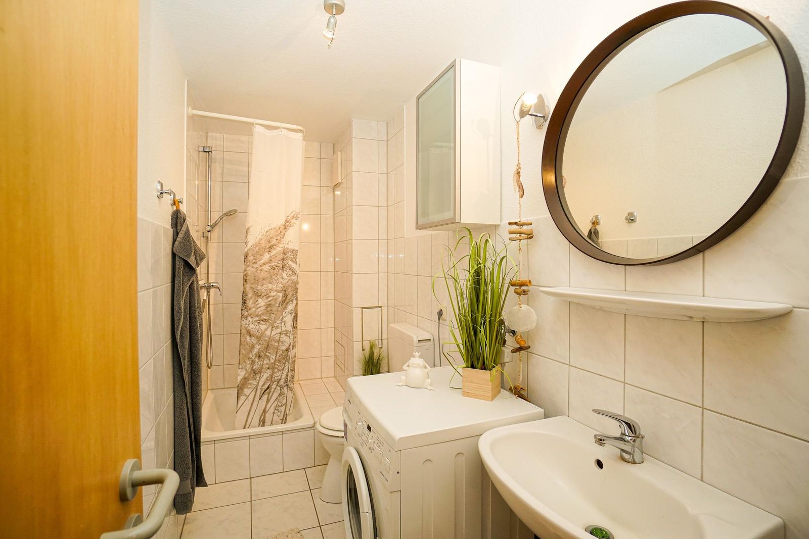 Badezimmer mit Dusche, Waschmaschine und Spiegel.