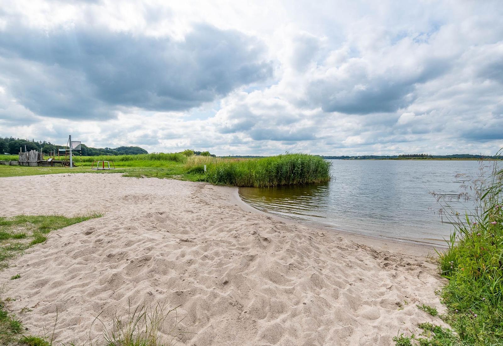 Strand mit Sand, Gras und Wasser unter bewölktem Himmel.