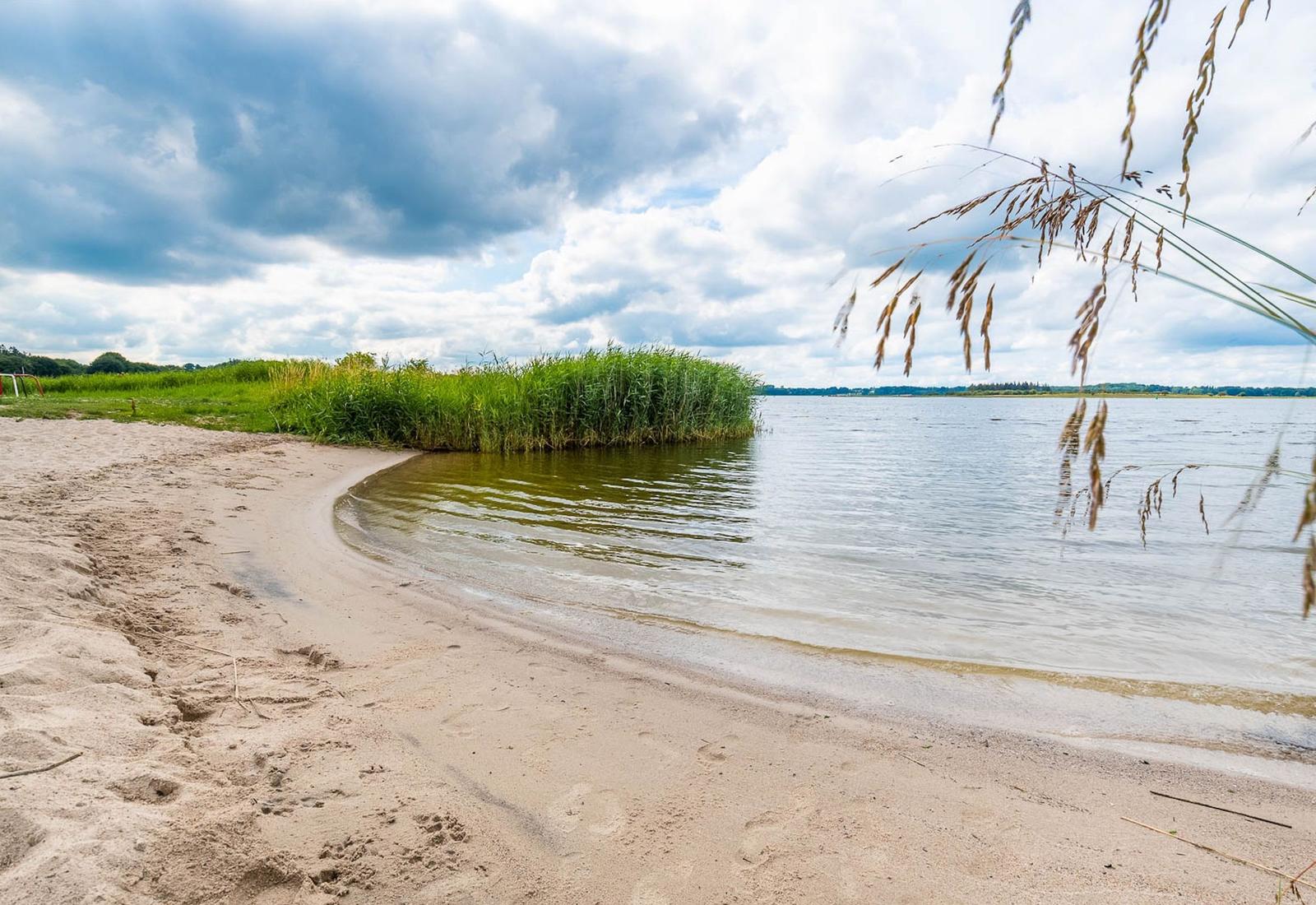 Strand mit Sand, Gras und Wasser unter bewölktem Himmel