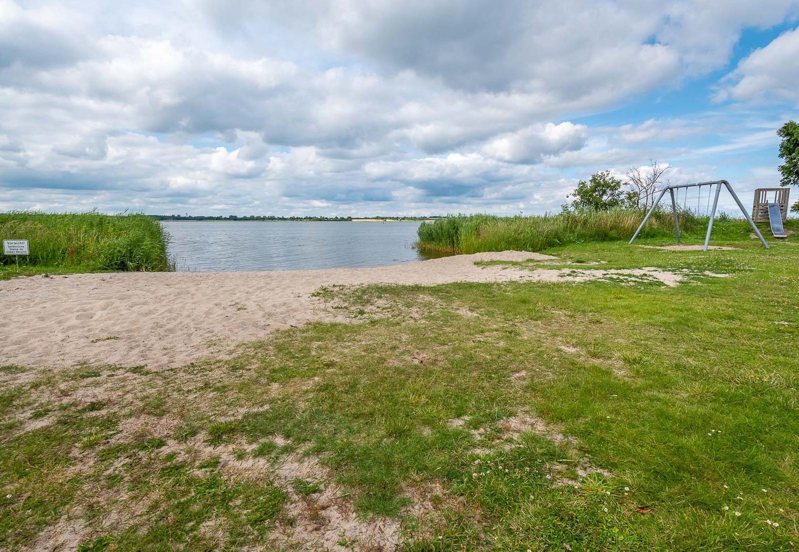 Strand mit Spielplatz am Ufer eines Sees unter bewölktem Himmel.