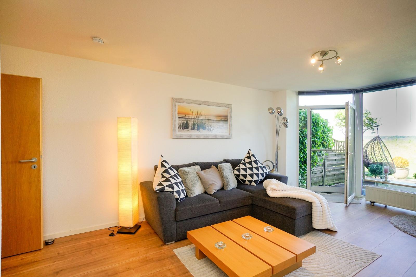 Ein Wohnzimmer mit grauem Sofa, Holztisch und Glasfront zur Terrasse.