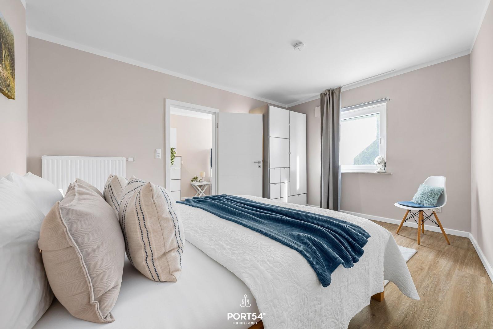 Schlafzimmer mit Bett, Kleiderschrank und Fenster. Holzboden und Wandfarbe.