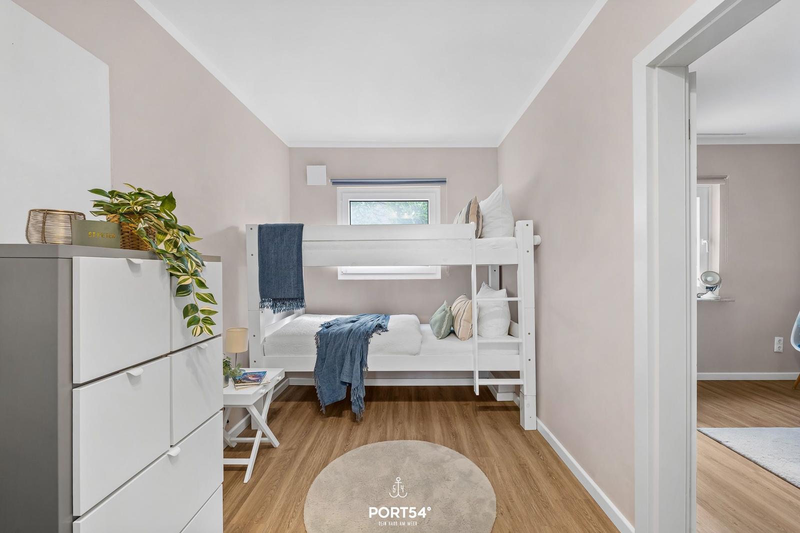 Schlafzimmer mit Doppelstockbett, Schrank und Fenster. Holzboden und runder Teppich.