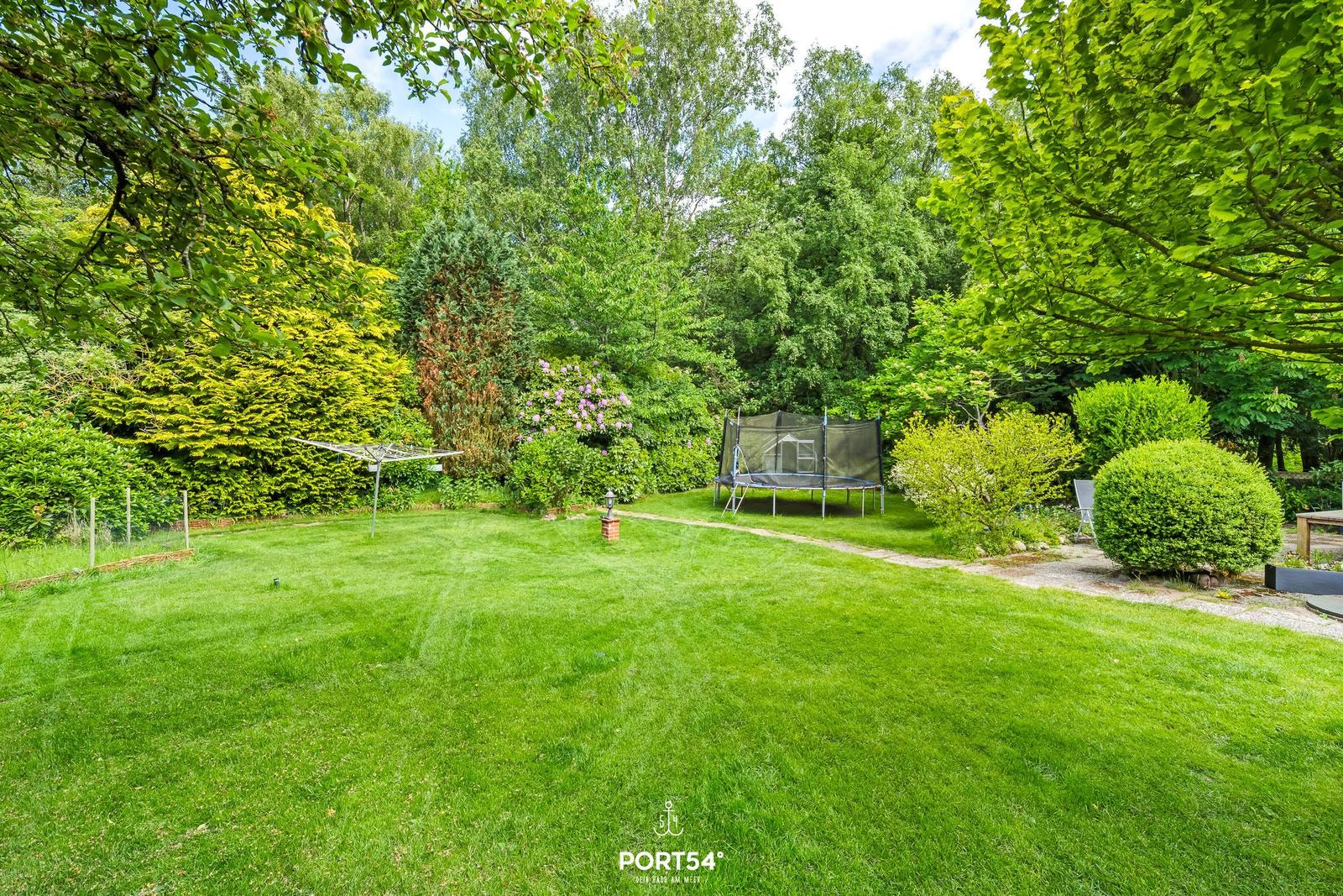 Großer Garten mit Trampolin, Grillplatz und umliegenden Bäumen.