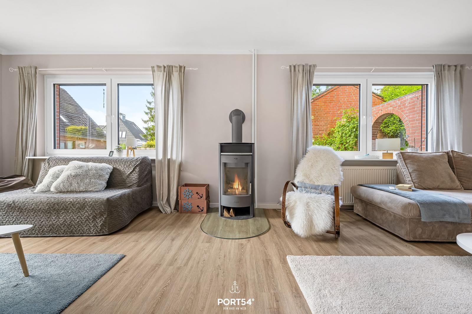 Wohnzimmer mit Kamin, Sofa und Sessel vor Fenstern mit Blick auf Garten.