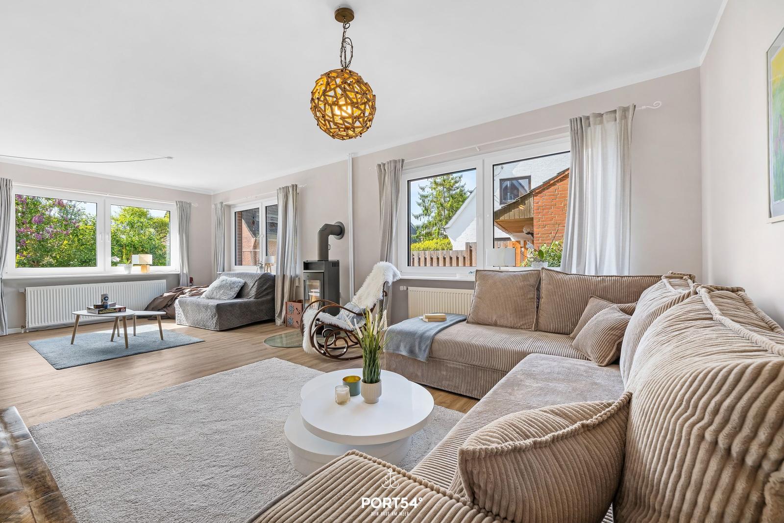 Wohnzimmer mit Sofa, Couchtisch und Fenstern. Holzboden und Deckenleuchte.