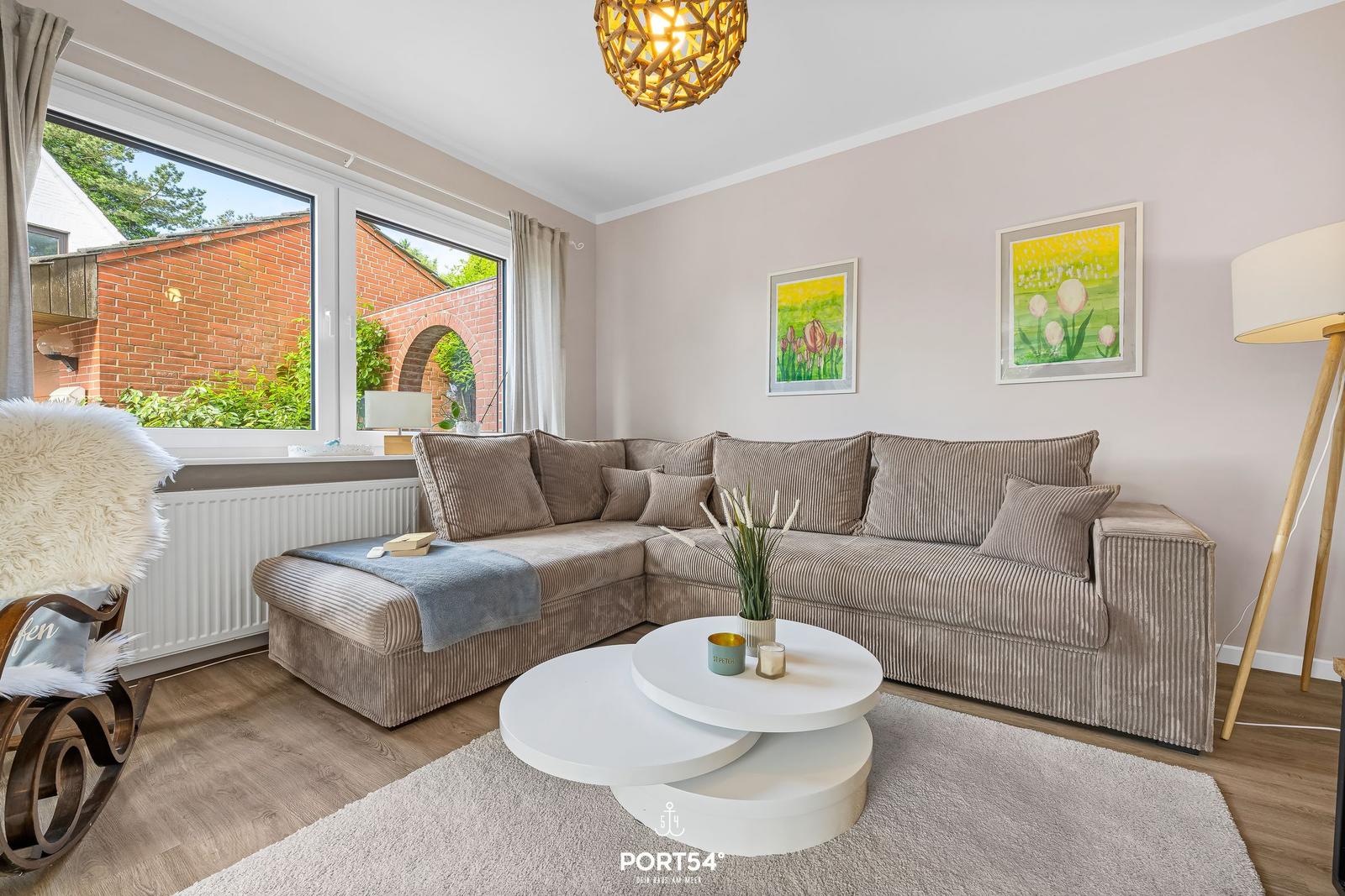 Wohnzimmer mit Ecksofa, runden Tisch und Fenster zum Garten.