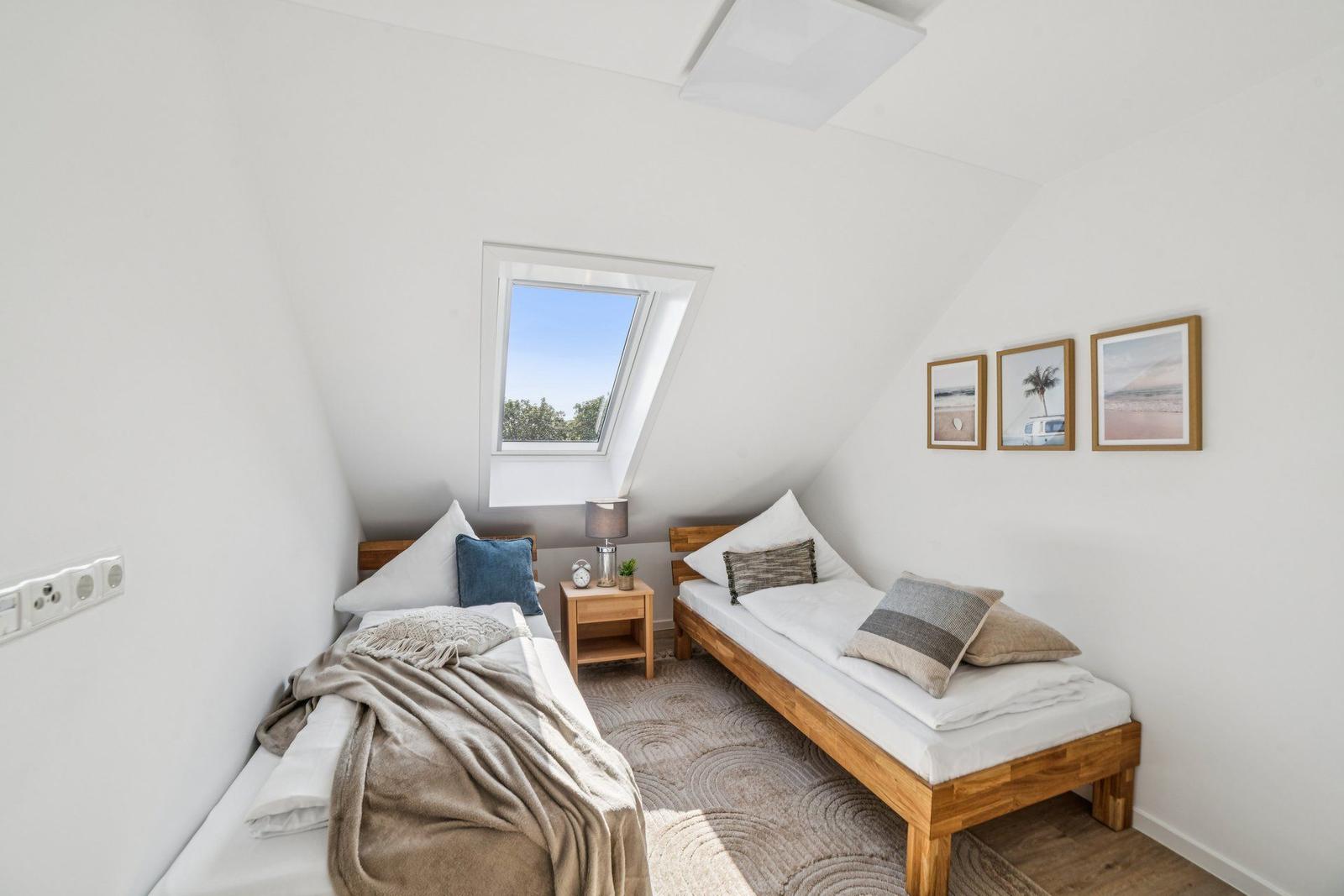 Zwei Betten in einem Dachzimmer mit Dachfenster und Wandbildern.