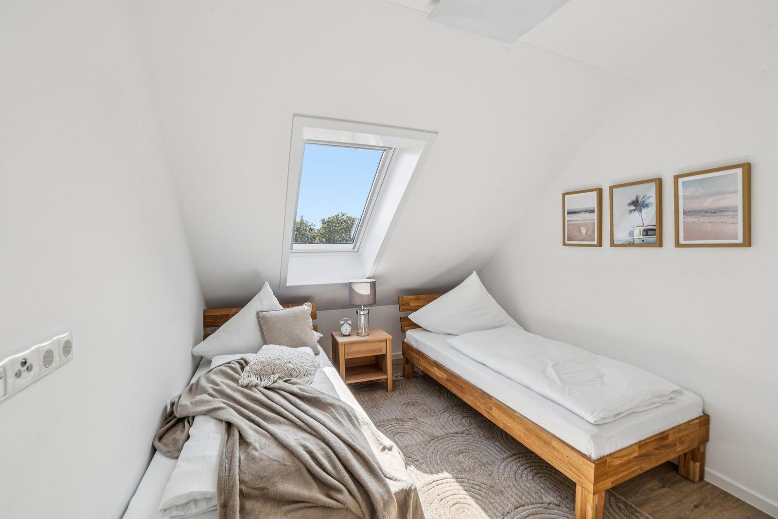 Zimmer mit zwei Betten, Dachfenster und Wandbildern.