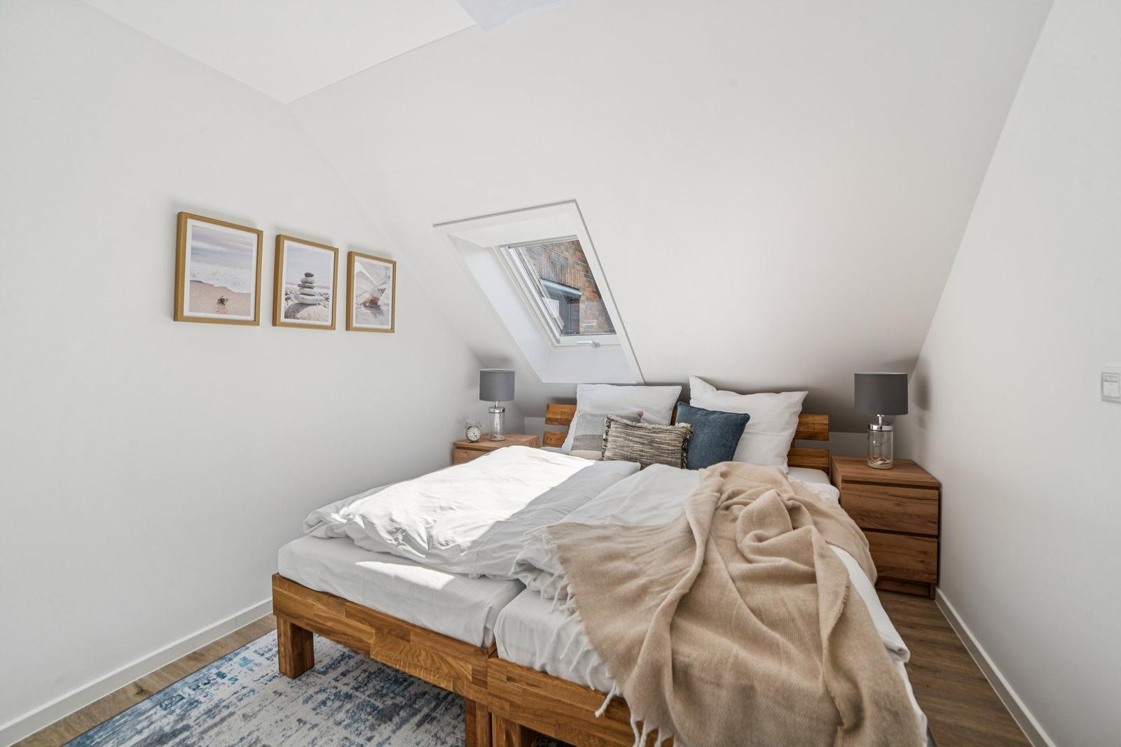 Schlafzimmer mit Dachschrägen, Dachfenster und Holzbett. An den Wänden hängen drei Bilder.