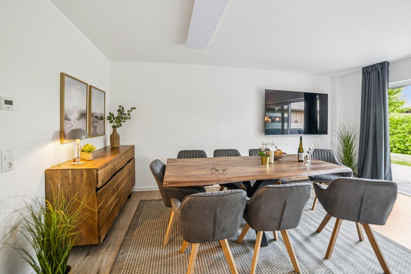 Esszimmer mit Holztisch, grauen Stühlen und Fernseher an der Wand.