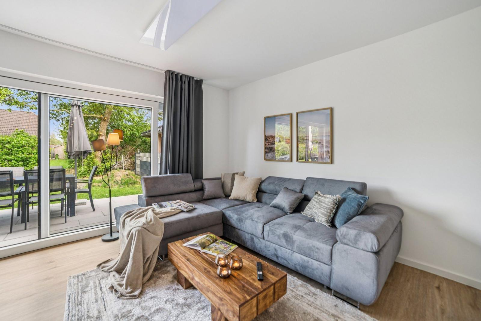 Wohnzimmer mit grauem Sofa, Holztisch und Blick auf die Terrasse.