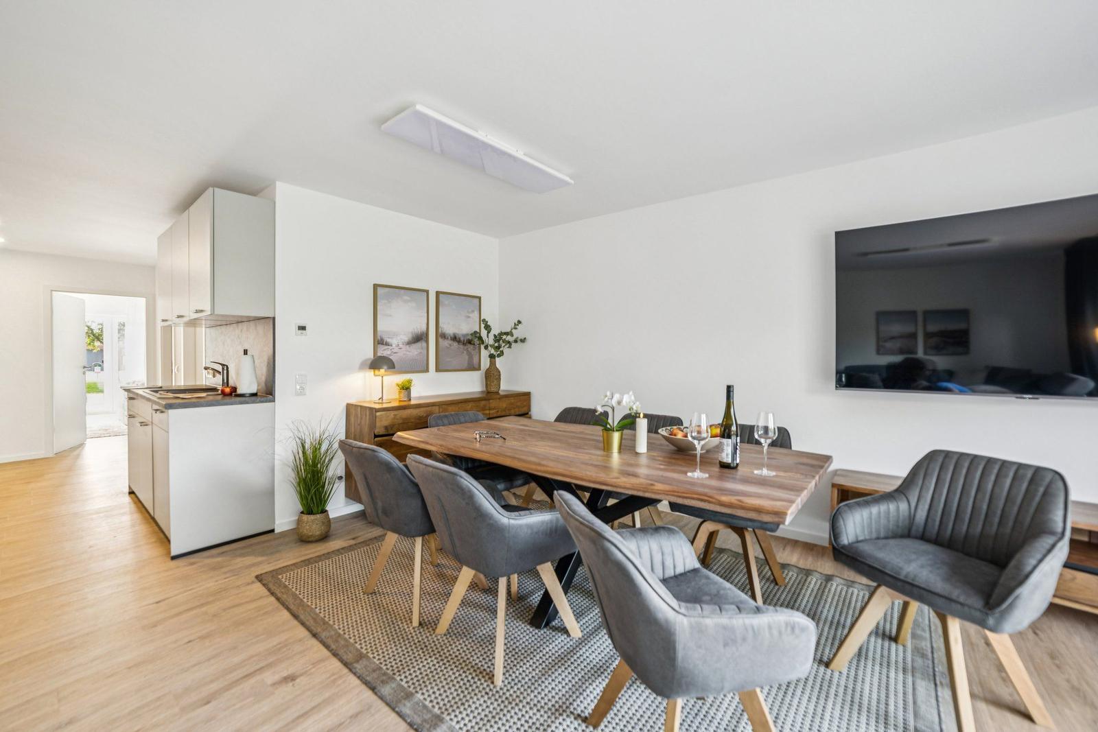 Essbereich mit Holztisch, grauen Stühlen und Fernseher an der Wand.