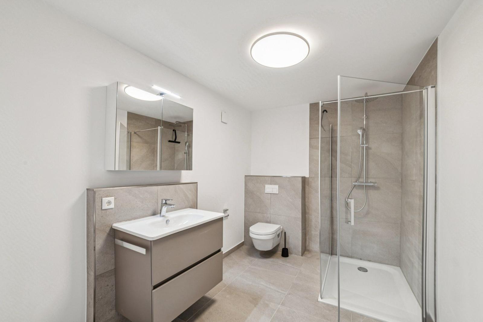 Badezimmer mit Dusche, Waschbecken und WC. Fliesen und Spiegel sichtbar.