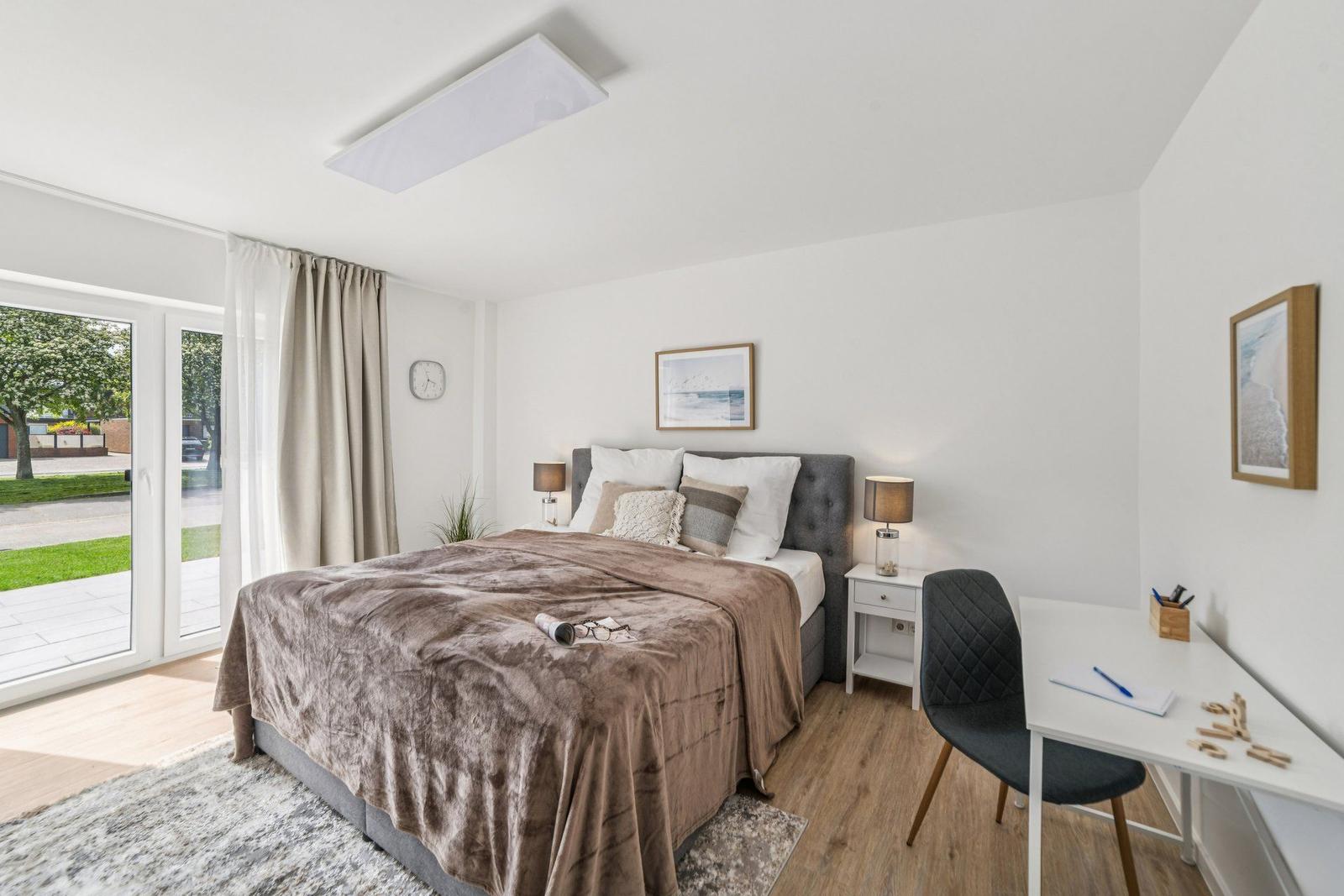 Schlafzimmer mit Bett, Schreibtisch und Glastür zur Terrasse.